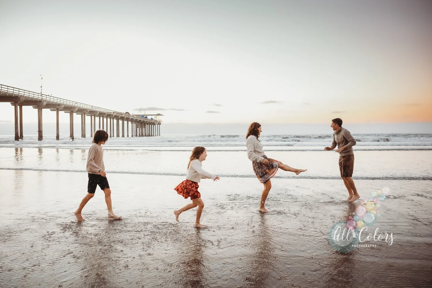 family playing on the beach splashing each other with the Scripps Pier in the back