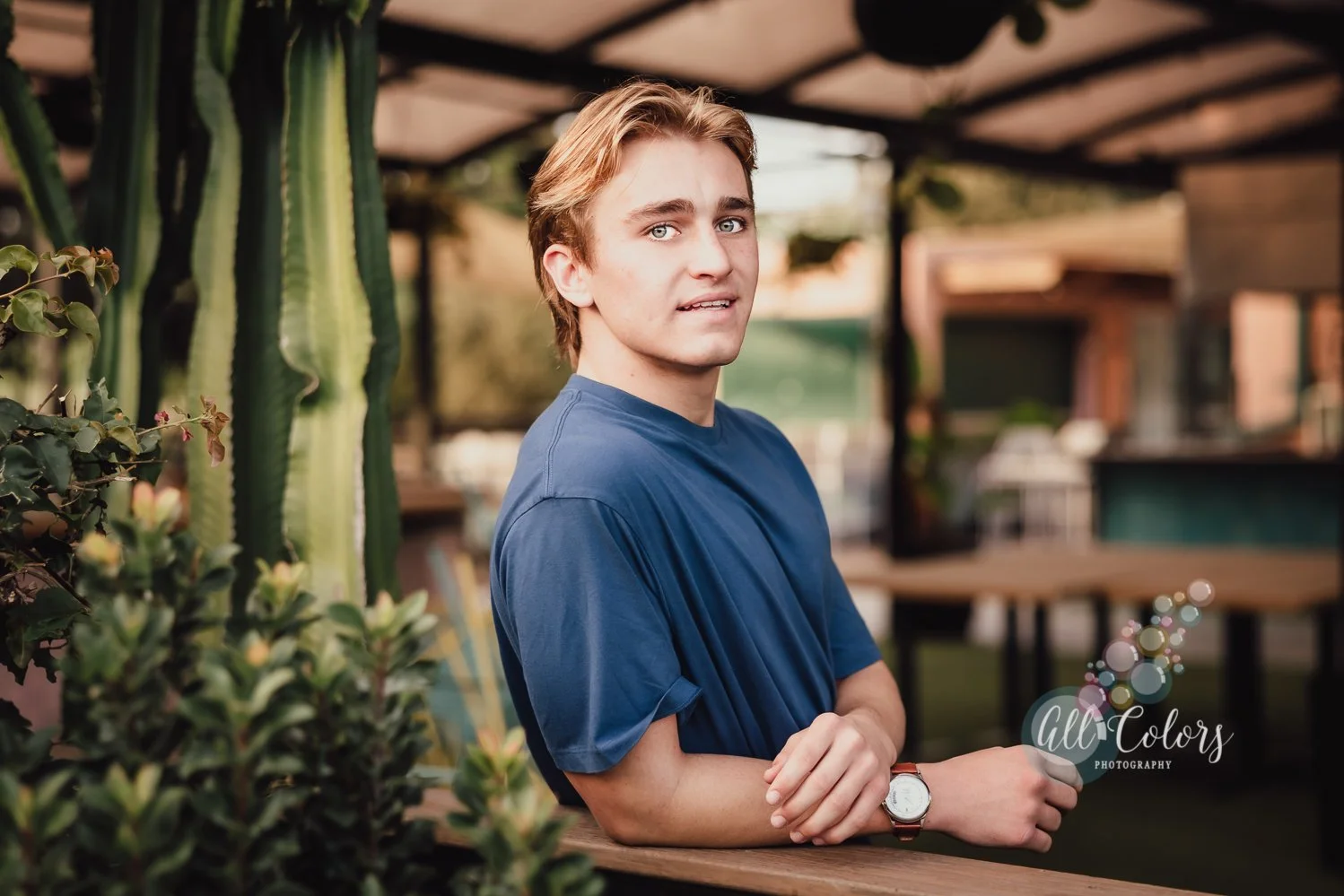 Young man wearing a blue shirt leaning on a fence