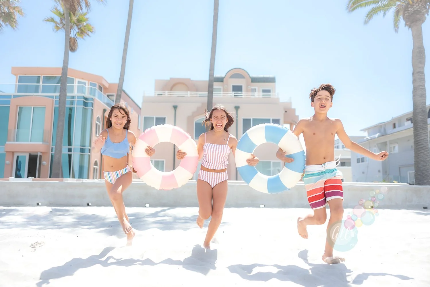 Three kids playing with pastel color floats at the beach