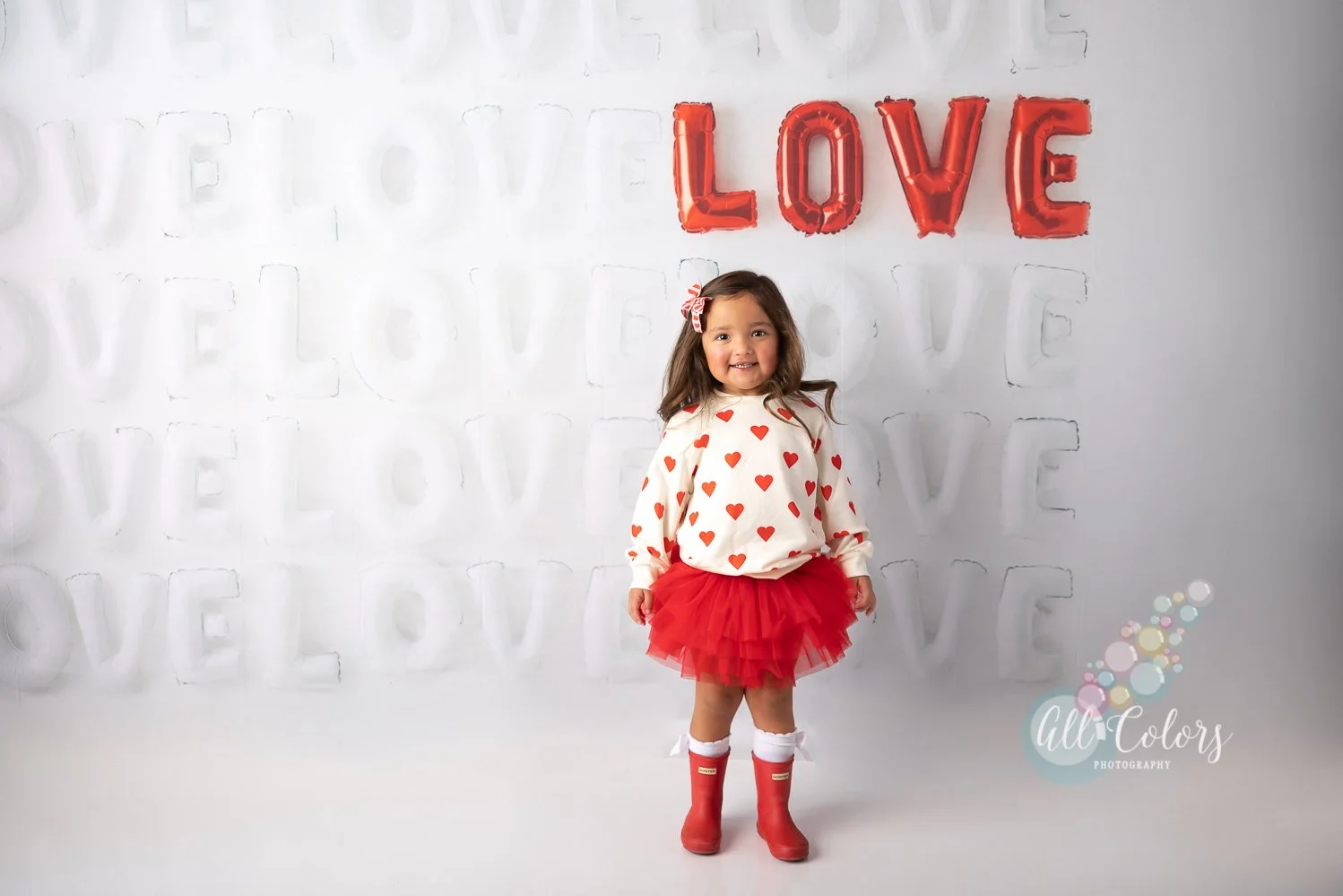 Little girl dressed up for Valentine's Day in front of a wall of LOVE balloons