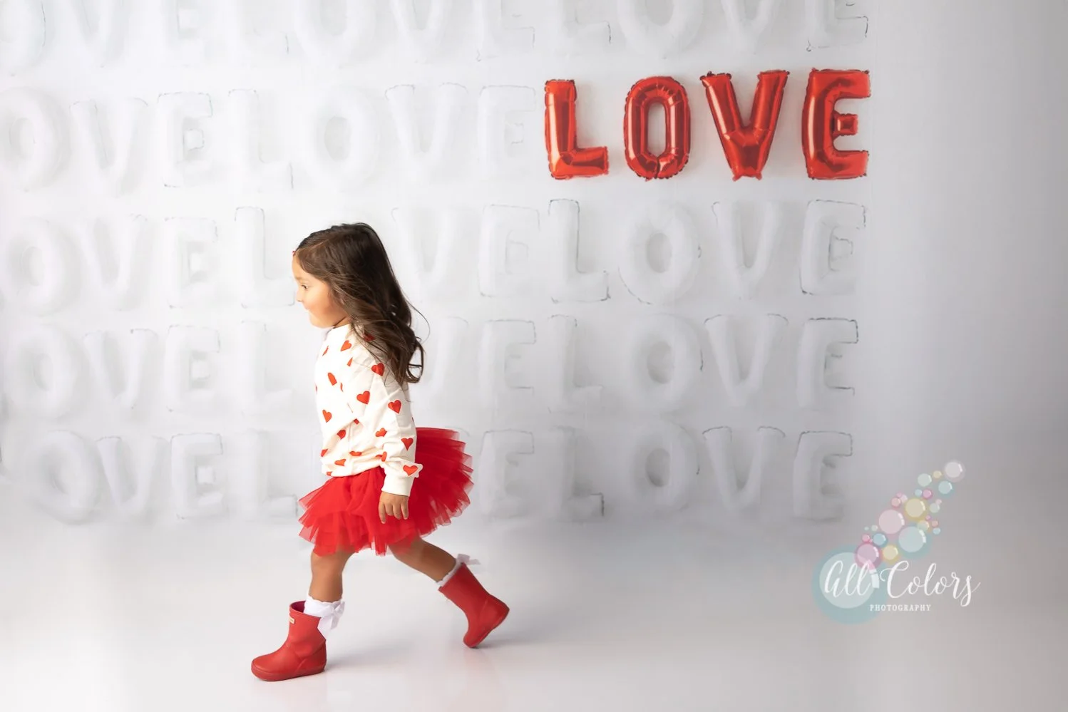 Little girl dressed up for Valentine's Day in front of a wall of LOVE balloons
