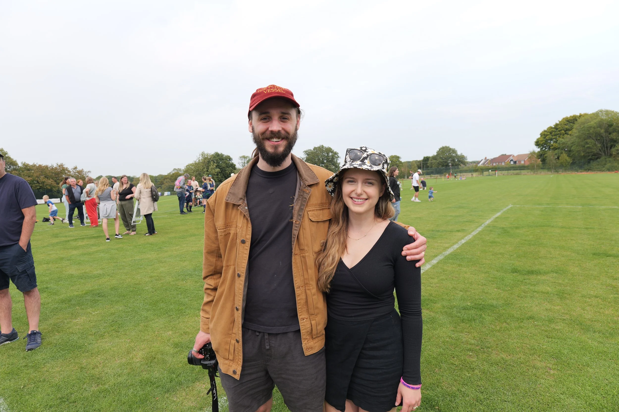 Rachael and Nathan Hassall, Malibu Poet Laureate Emeritus and Founder of The Poetry Vessel, pictured a park or sports field, with a crowd of people in the background.
