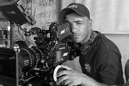 A man with a cap operating a professional ARRI camera on a film set.