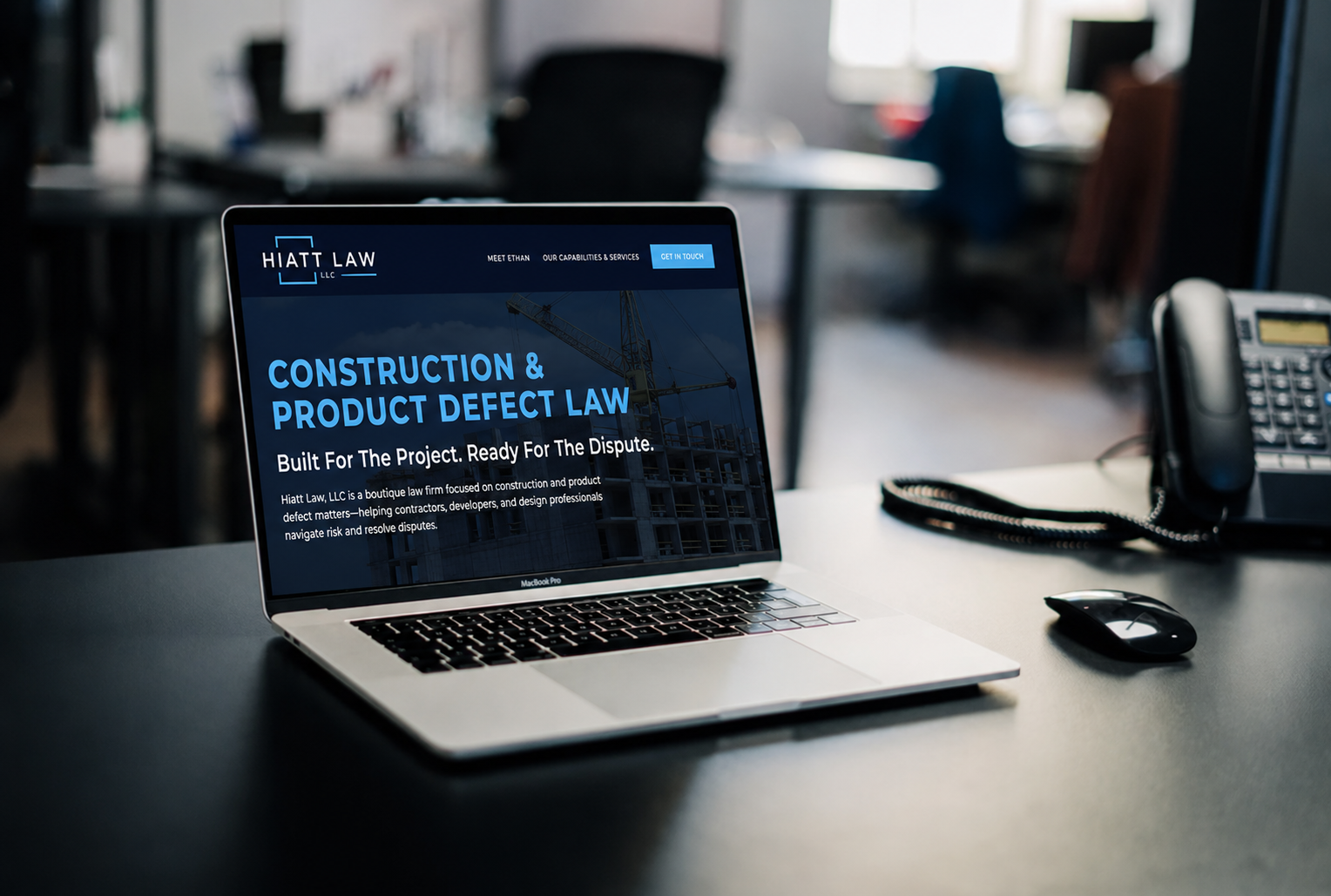 A laptop on a desk displaying the homepage of Hiatt Law LLC, a law firm specializing in construction and product defect law, with a partially visible landline phone and mouse nearby.