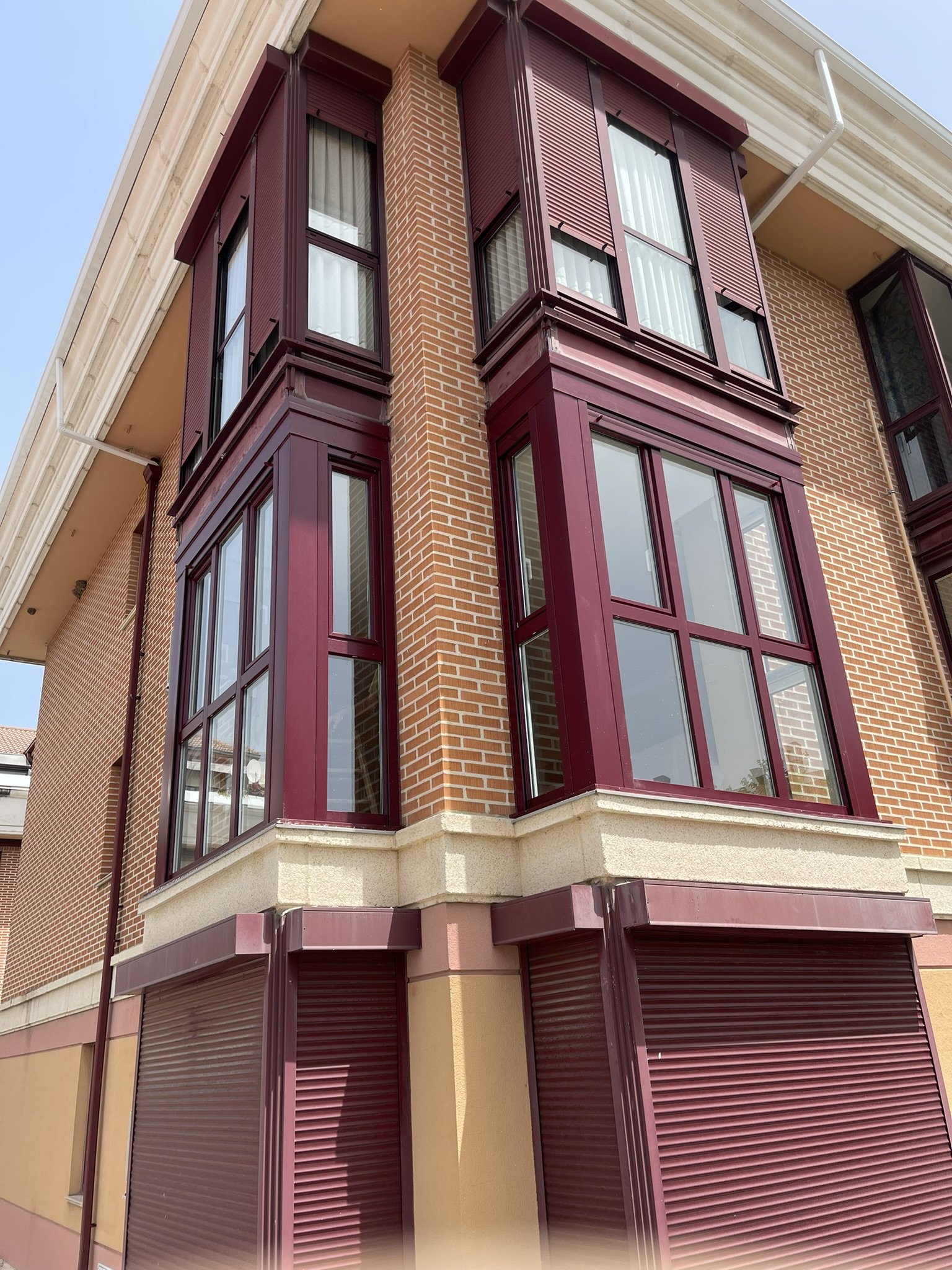 Edificio con ventanas de vidrio y persianas moradas en una esquina en un día soleado.