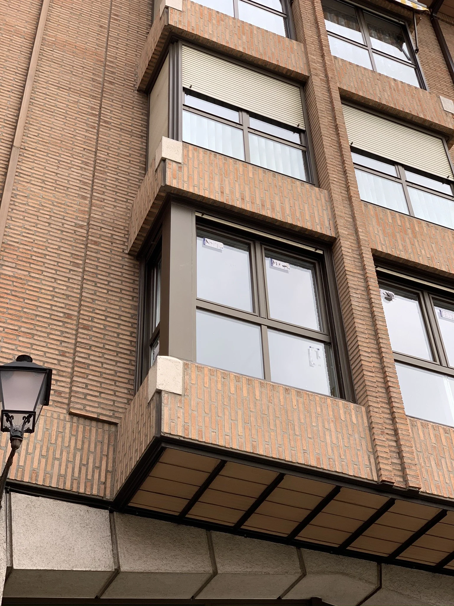 Vista de un edificio con paredes de ladrillo, varias ventanas con persianas y balcones, y un farol en la parte inferior izquierda.