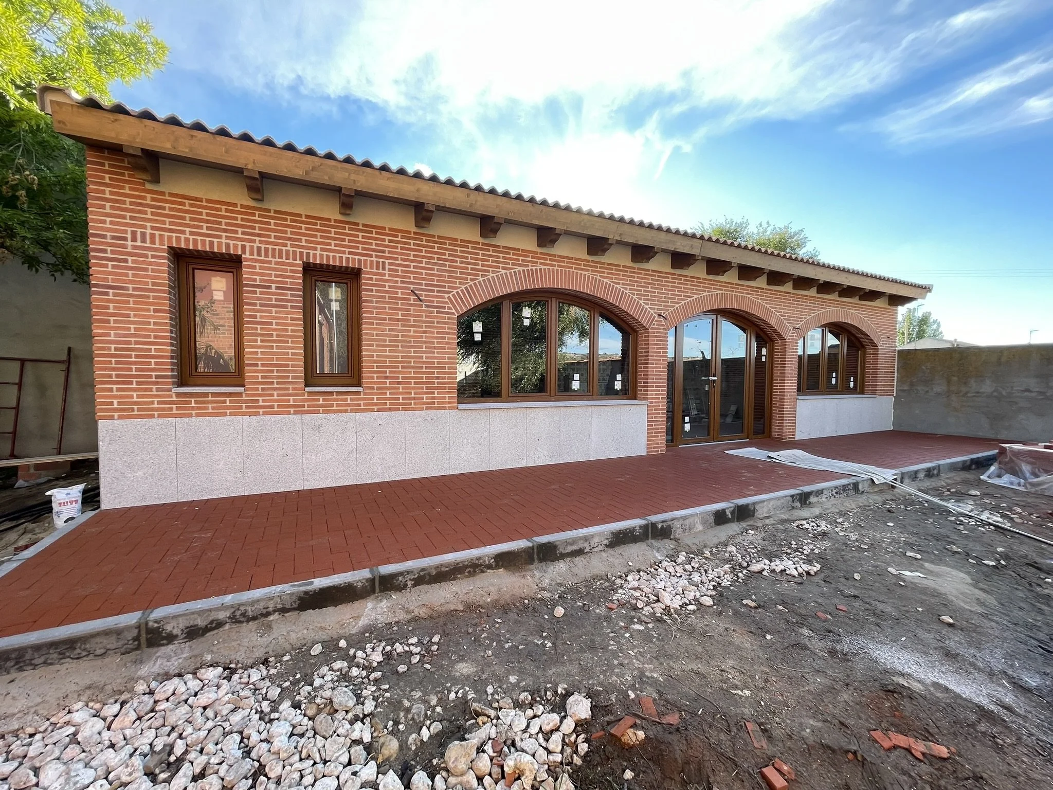 Construcción de una casa con paredes de ladrillo y ventanas de madera, con un techo de tejas y un camino de ladrillos en un día soleado.