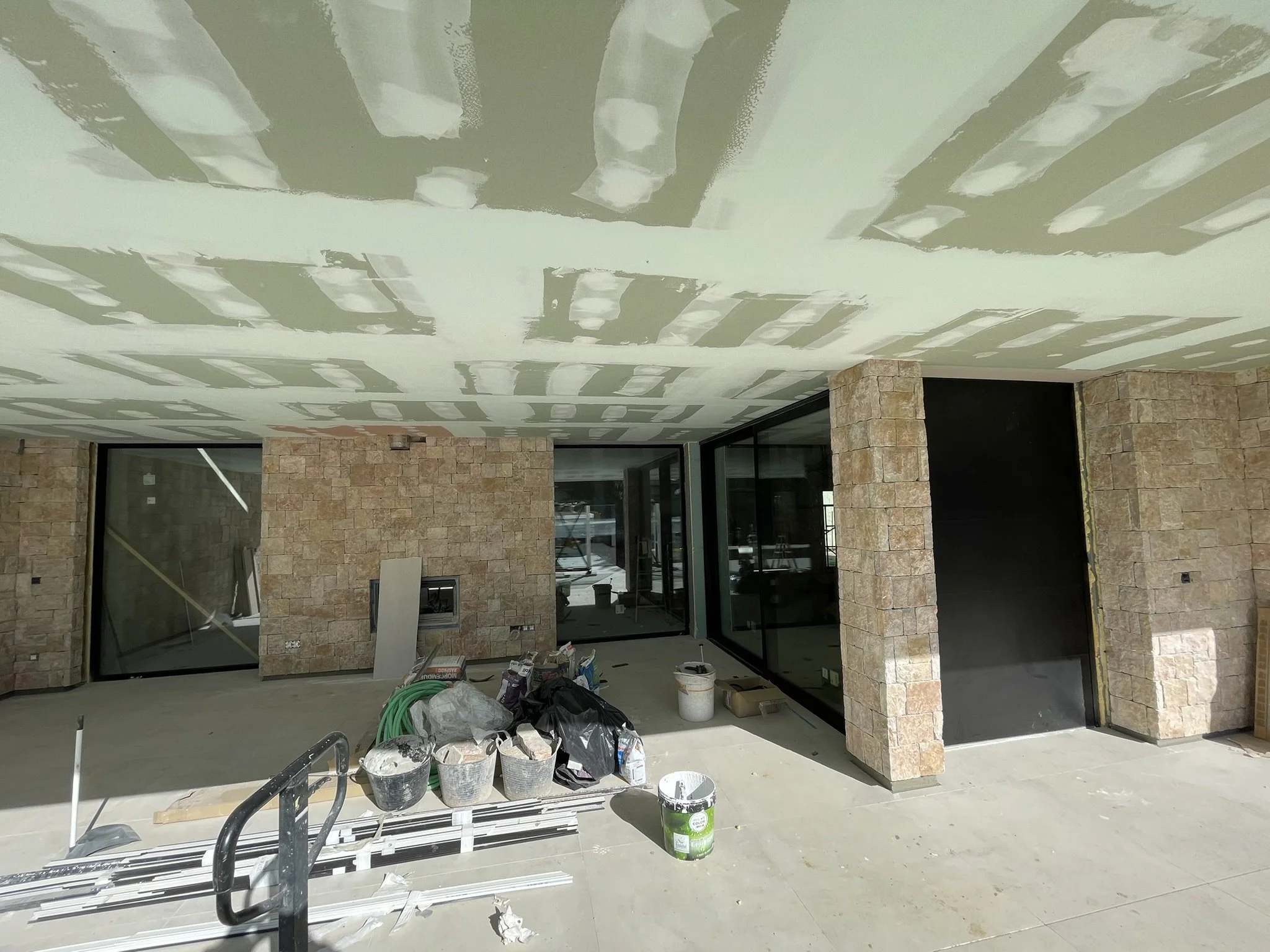 Construcción interior de un edificio con trabajos en curso, paredes de ladrillo y techos con suspensión en proceso, herramientas y materiales de construcción distribuidos en el área.
