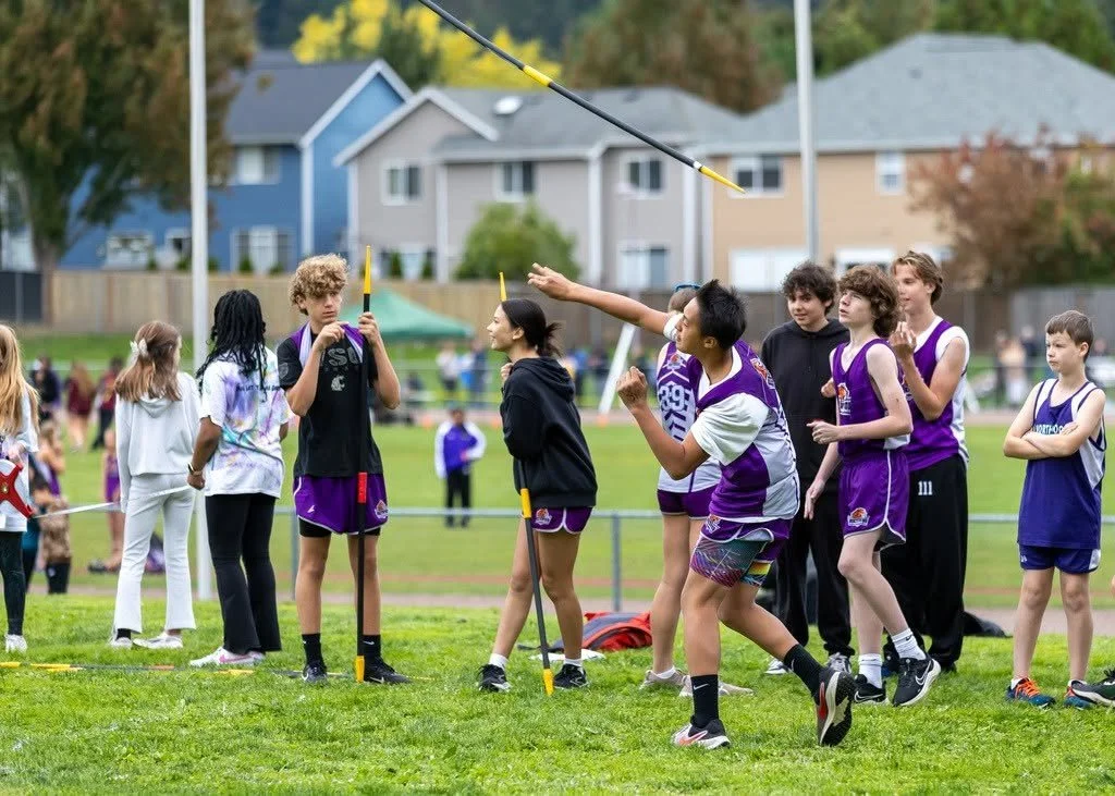 Children and teenagers competing in a javelin throw event on a grassy field.
