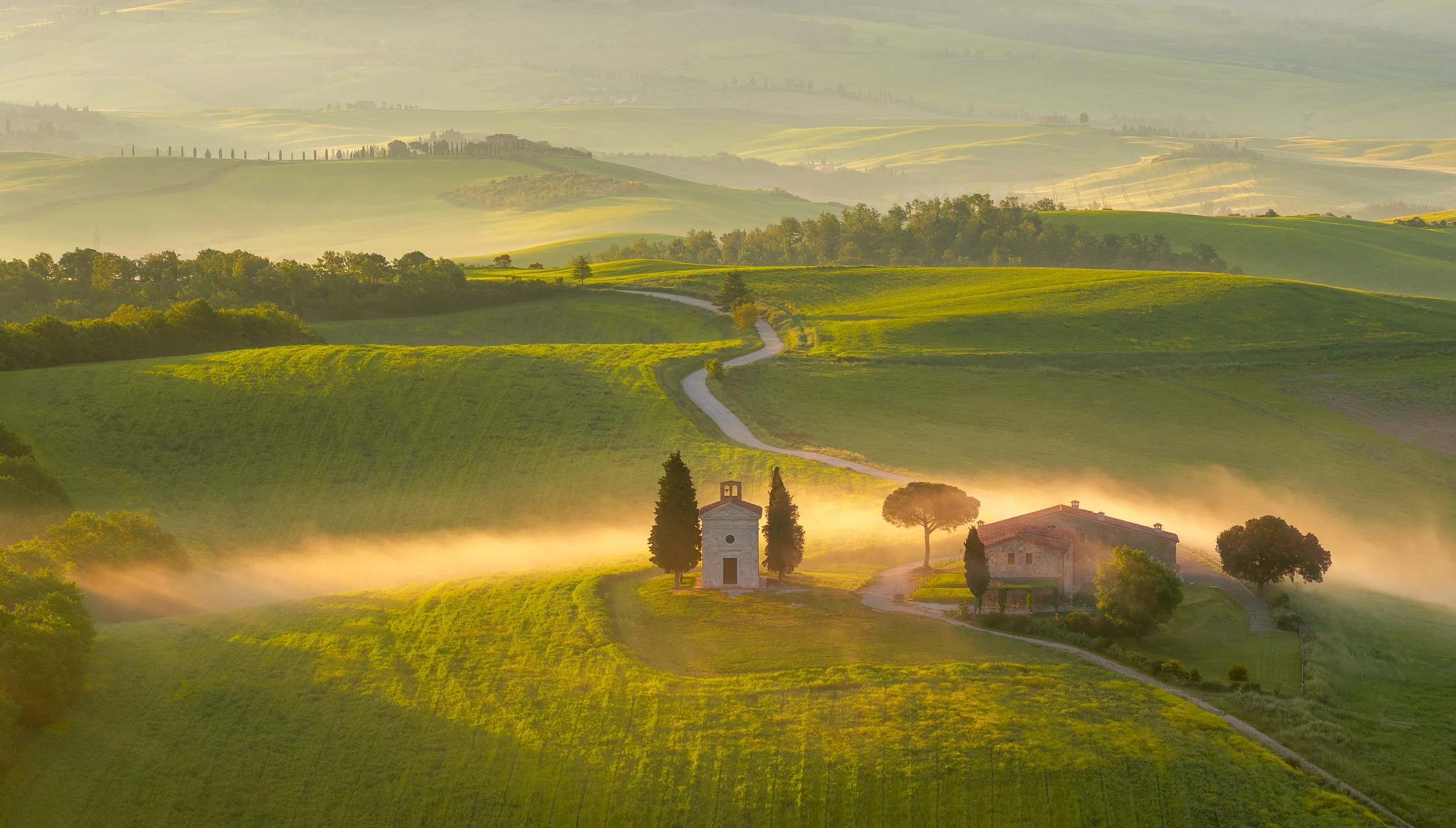 Aerial andscape photograph of fog surrounding Cappella della Madonna di Vitaleta, Val d'Orcia, Tuscany, Italy at sunrise.