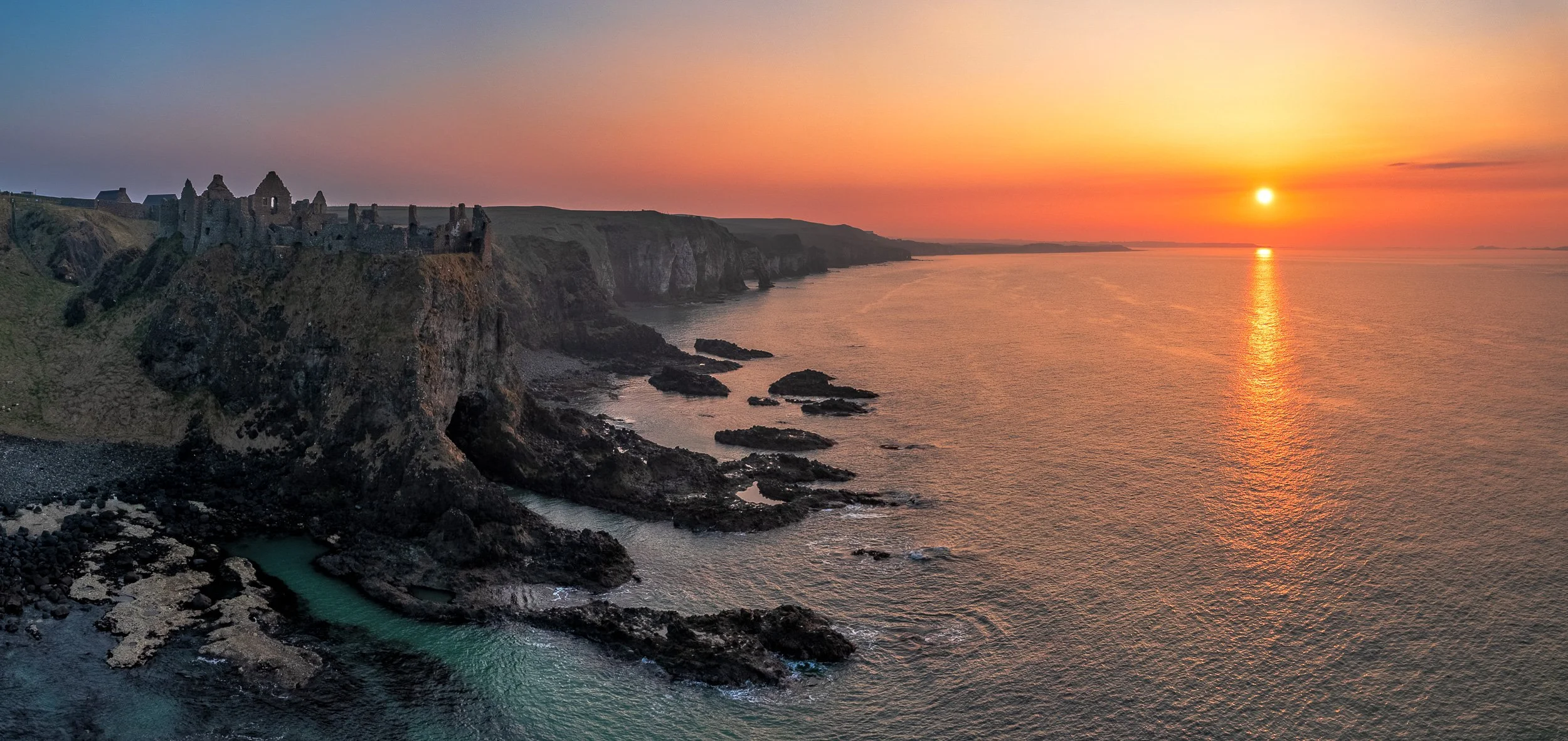 Aerial landscape photograph of Dunluce Castle, Northern Ireland at sunset.