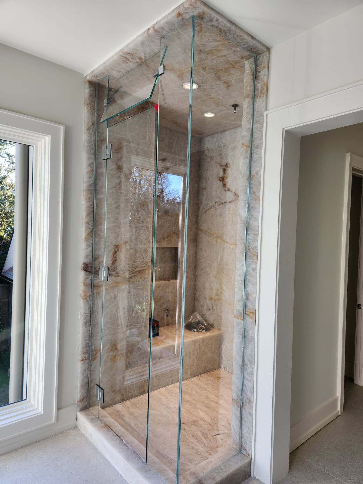 A modern walk-in shower with glass doors and marble walls in a bright bathroom.