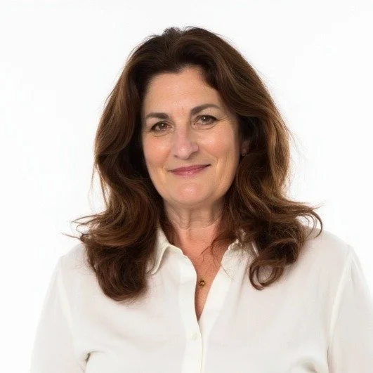 A woman with brown, shoulder-length wavy hair wearing a white blouse, smiling at the camera with a plain white background.
