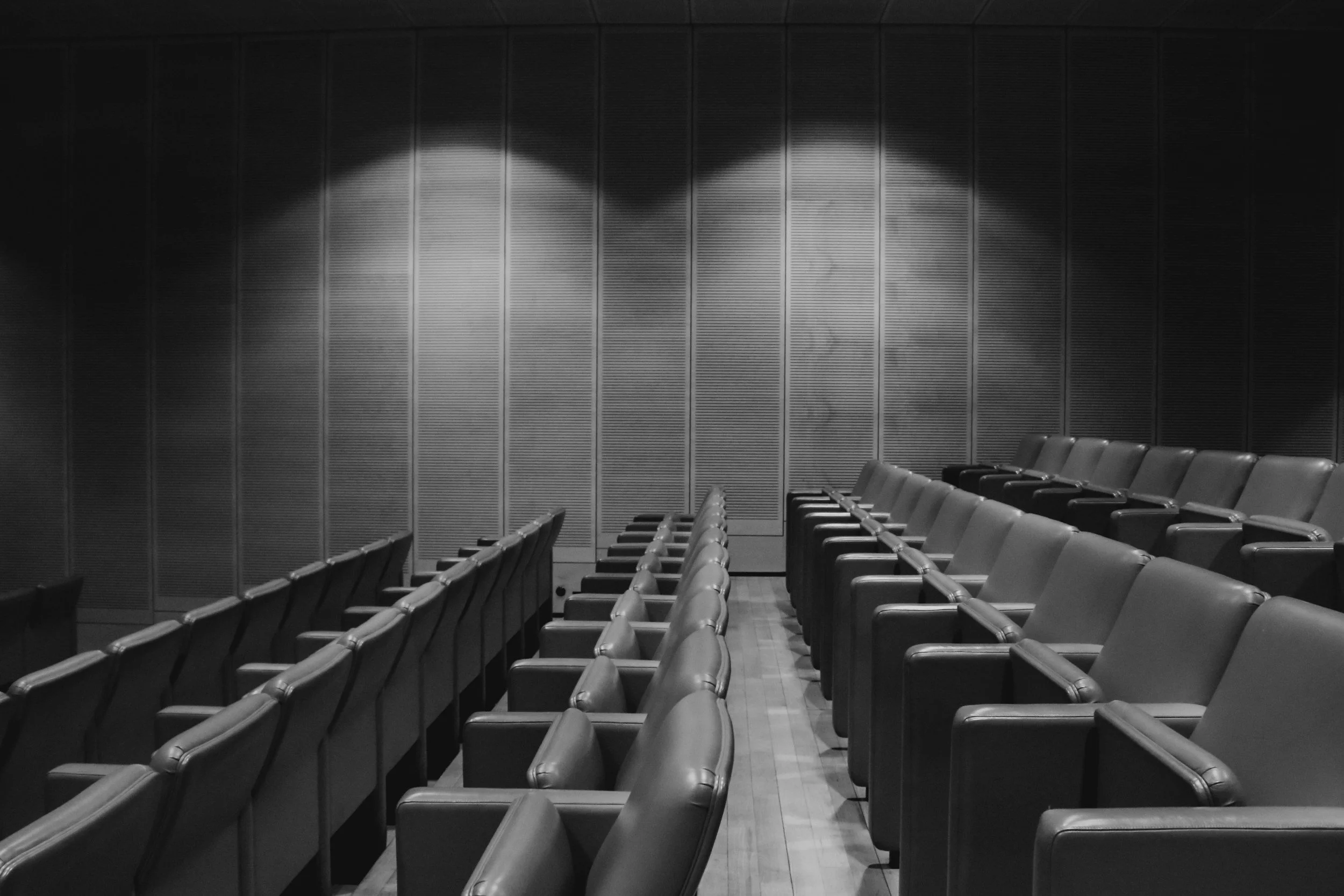 Empty auditorium with multiple rows of chairs and a textured wall with light patterns.