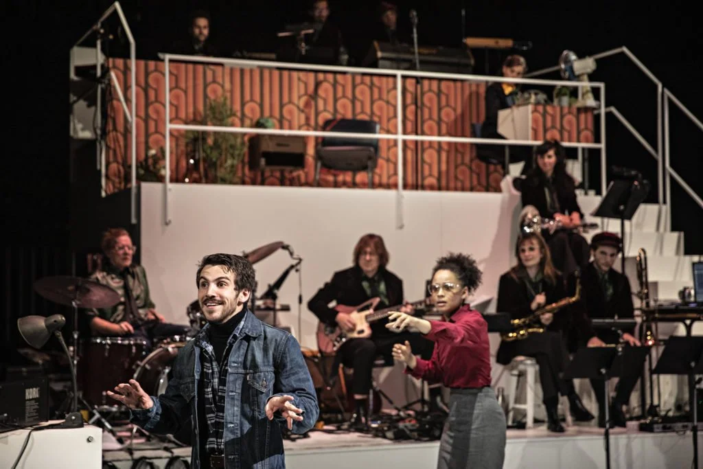A group of musicians performing on stage with a man and woman dancing in the foreground.