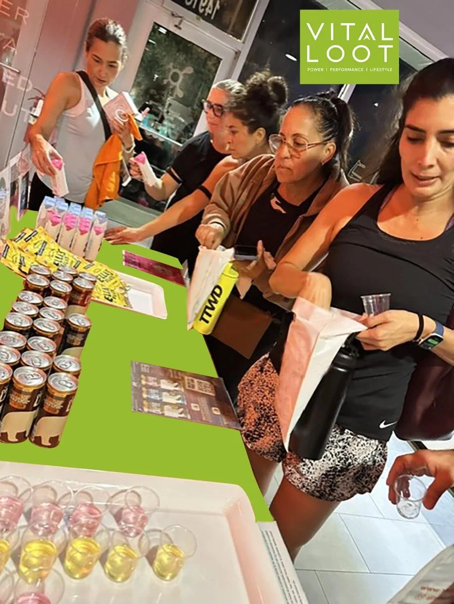 People shopping for energy drinks and snacks at a retail store counter with a green Vital Loot sign overhead.