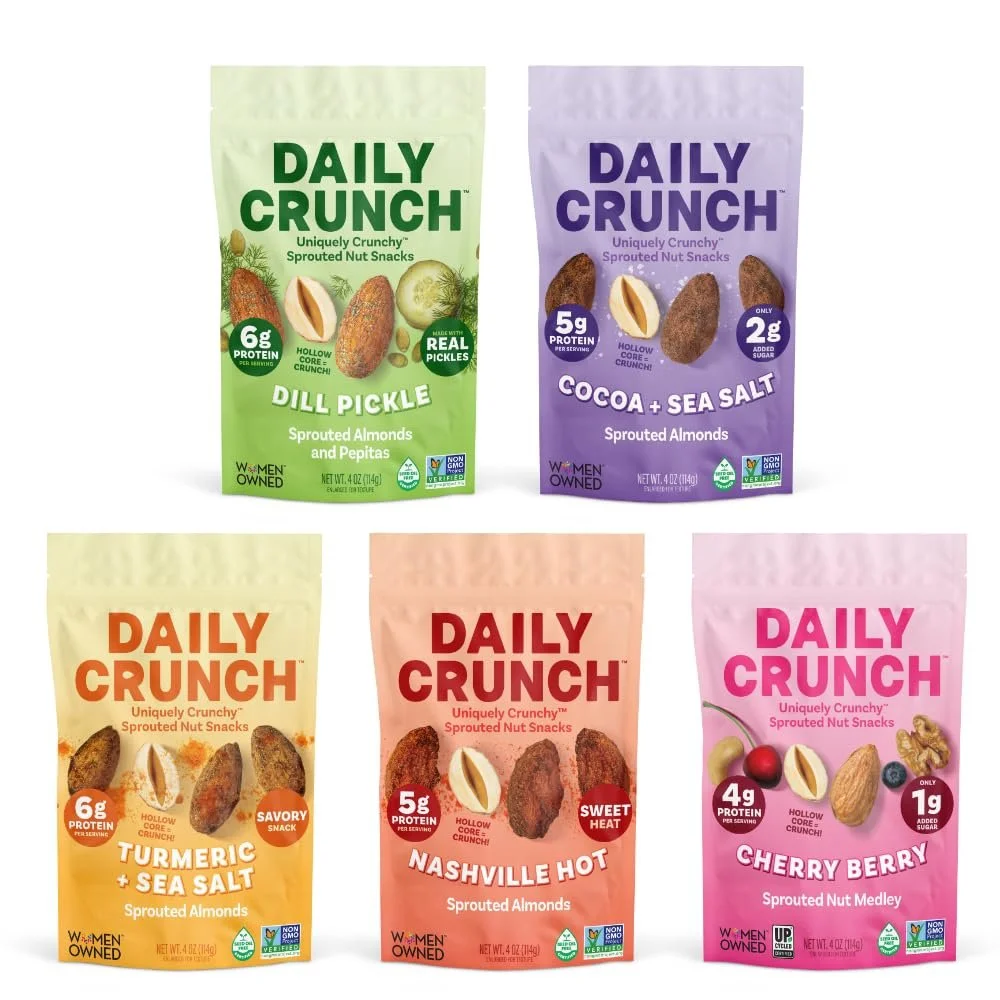 Five different flavors of Daily Crunch sprouted nut snacks in colorful packaging, including Dill Pickle, Cocoa + Sea Salt, Turmeric + Sea Salt, Nashville Hot, and Cherry Berry.