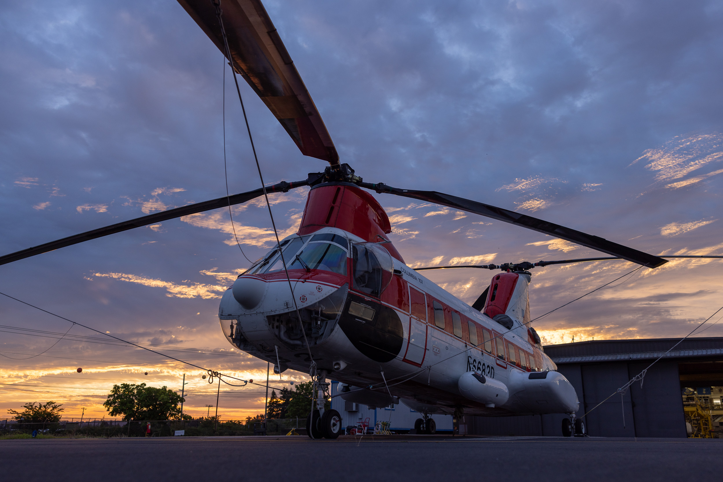 A helicopter parked on the tarmac during sunset with a partly cloudy sky in the background.