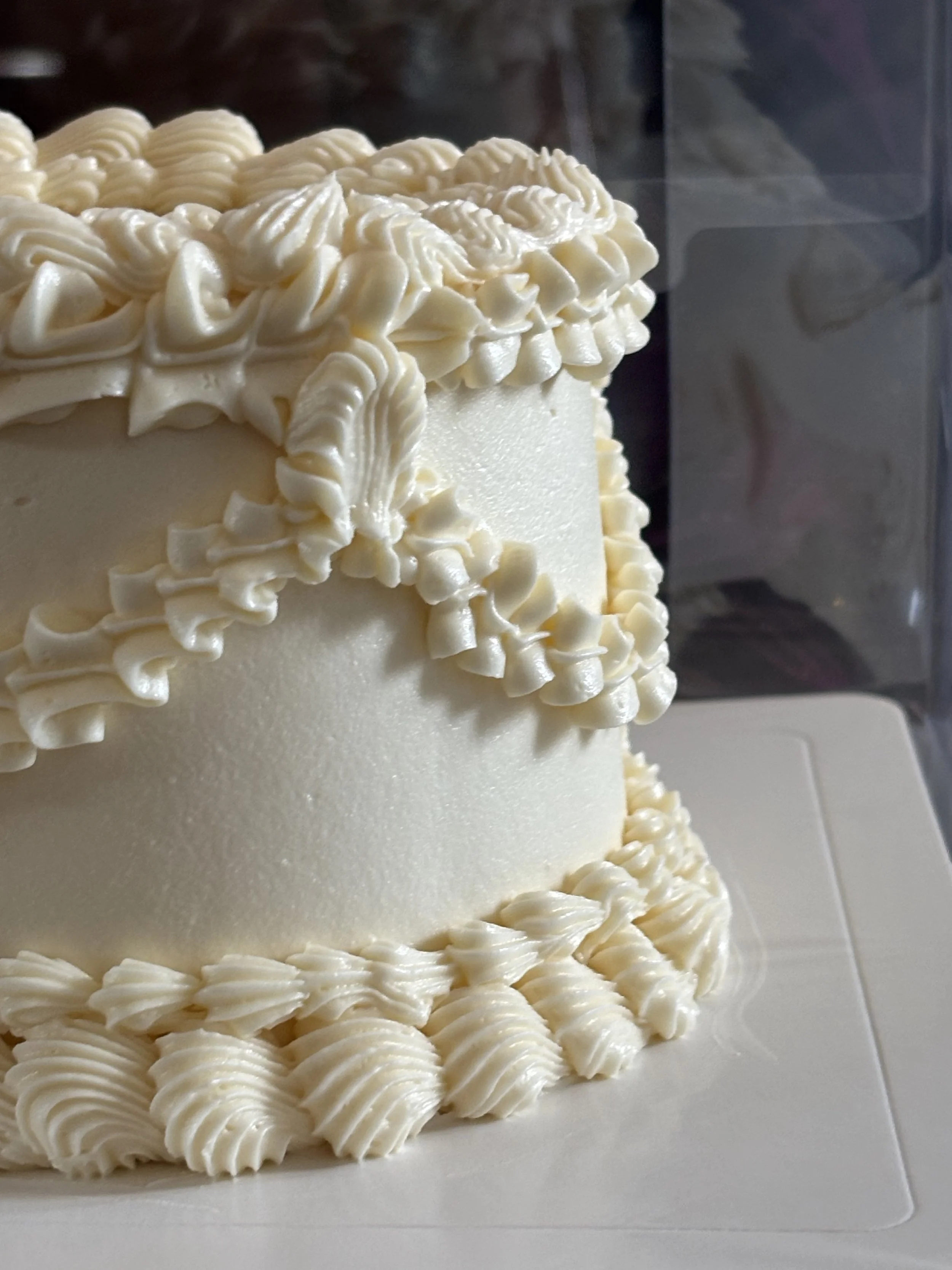 Close-up of a white frosted cake decorated with piped frosting swirls and rosettes.
