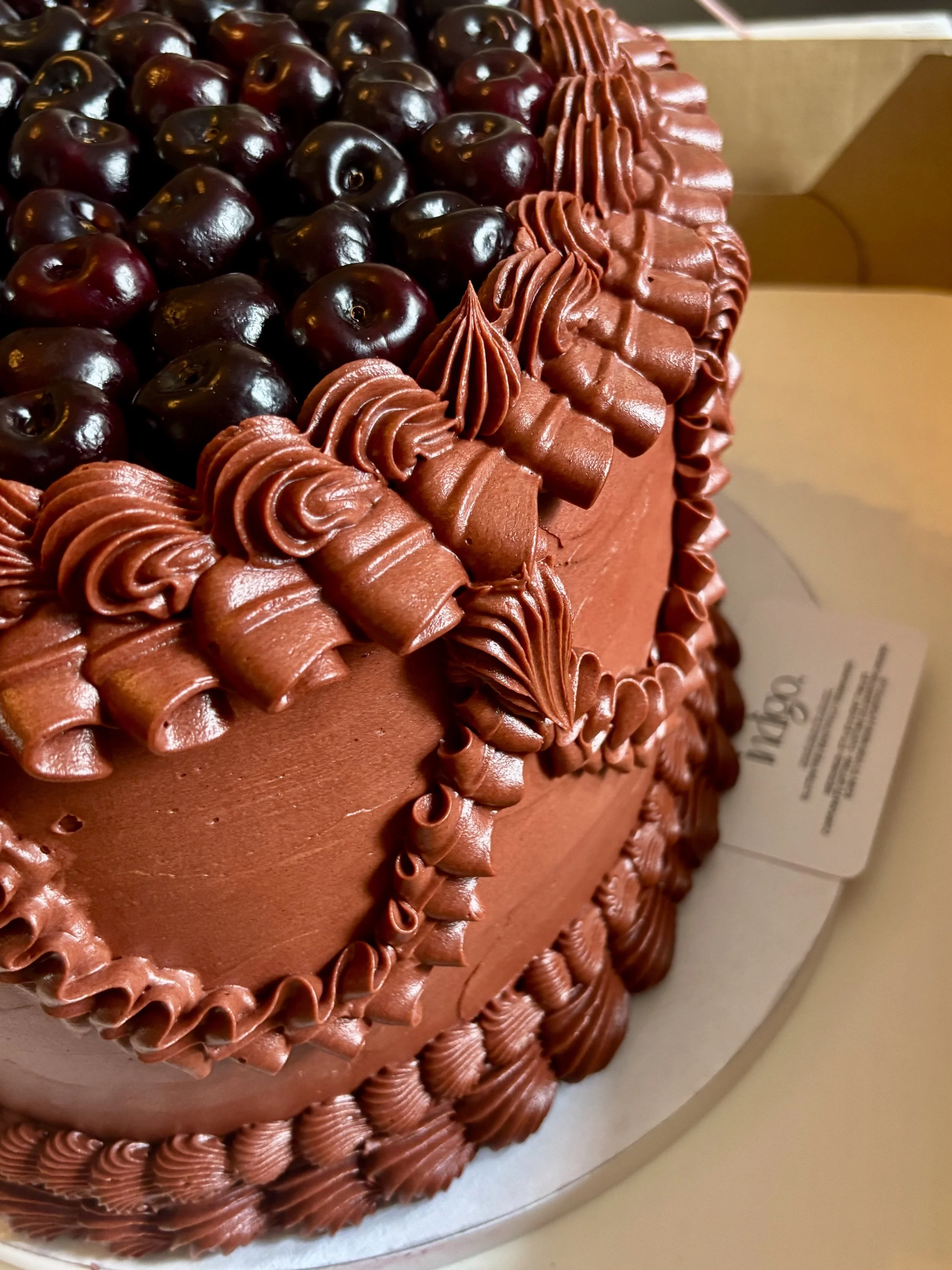 A close-up view of a luxe oval red cake decorated with cherries and piped vintage frosting details.