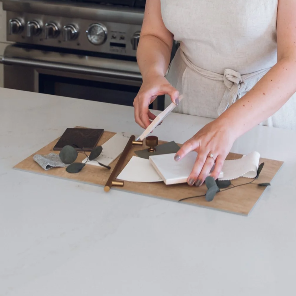 Person arranging decorative tiles and materials on a wooden board in a kitchen.