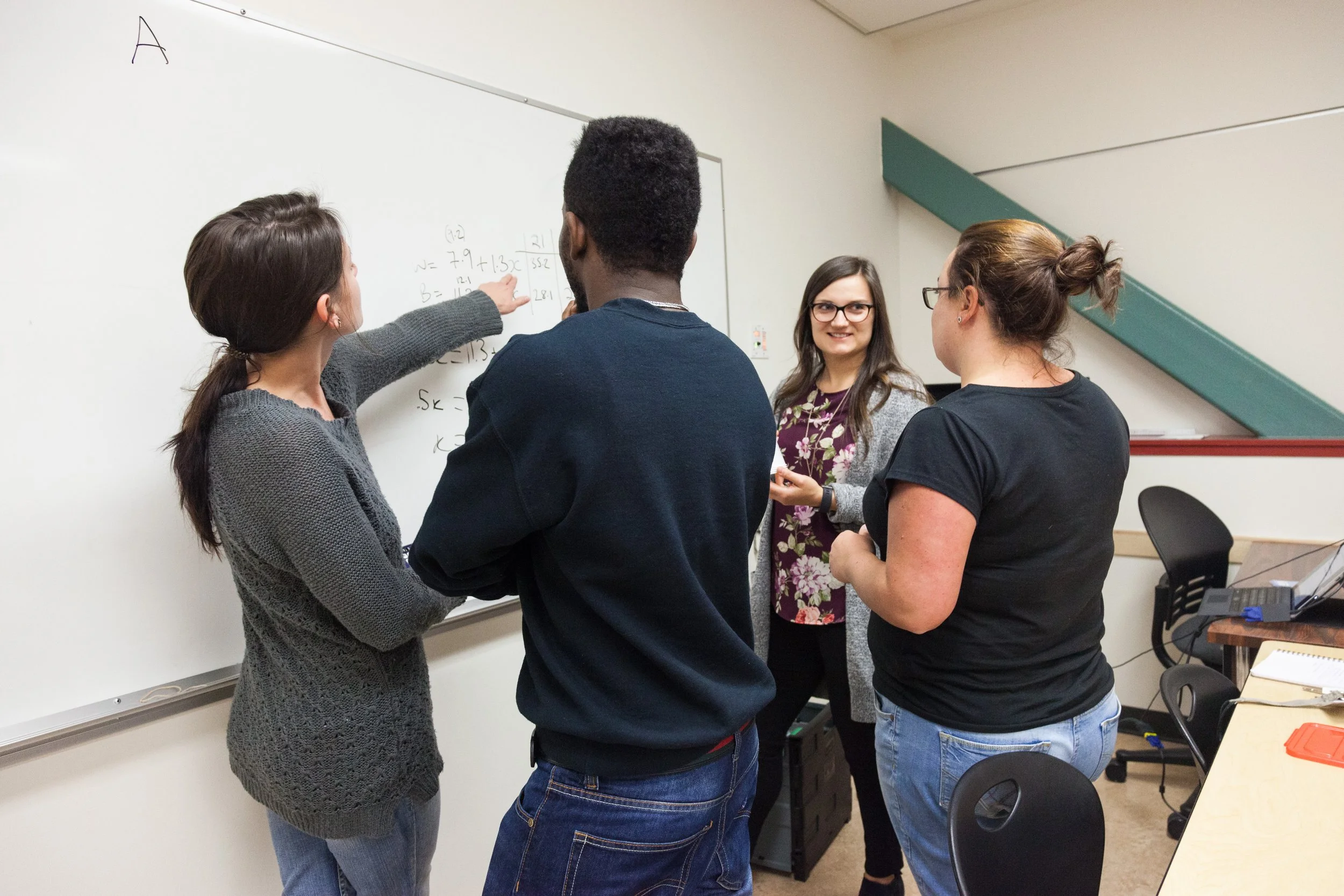 Group of students in a classroom around a whiteboard with mathematical equations.