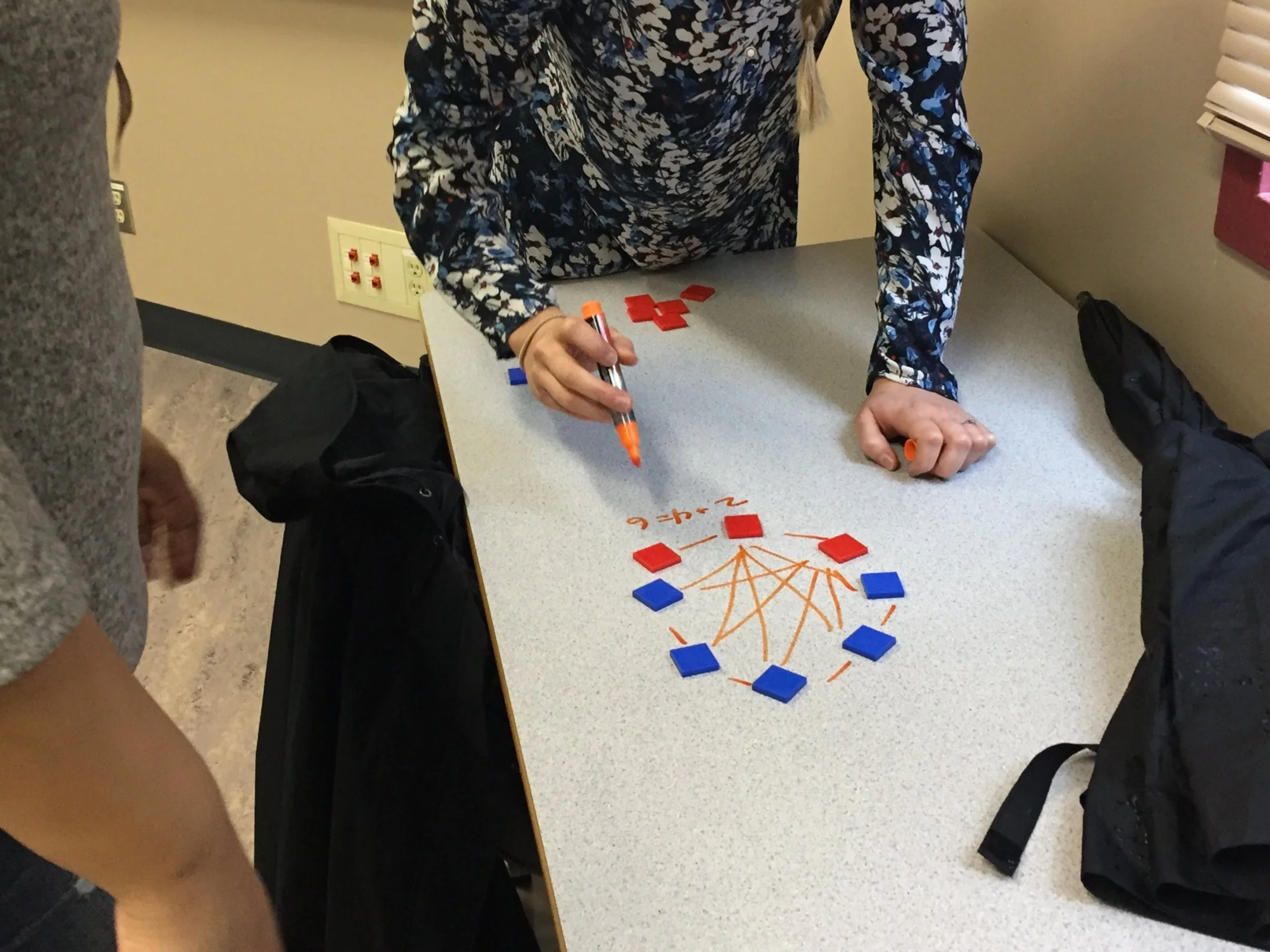 People gathered around a table playing a game with red and blue tiles connecting with orange drawn lines.