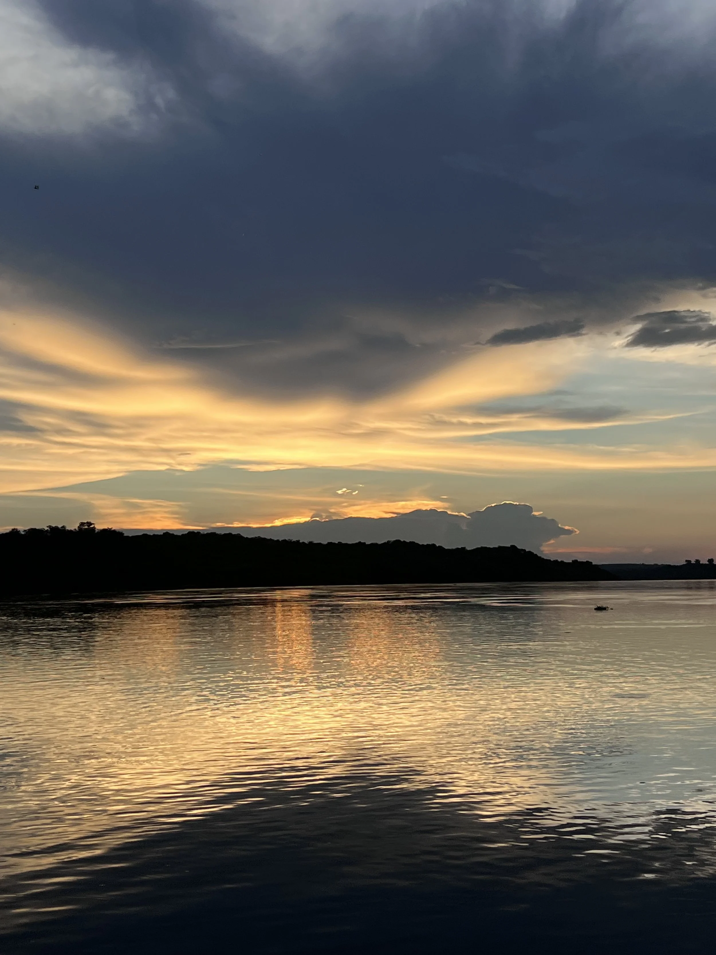 Sunset over the River Nile in Uganda, with golden light reflecting on the water beneath dramatic clouds.