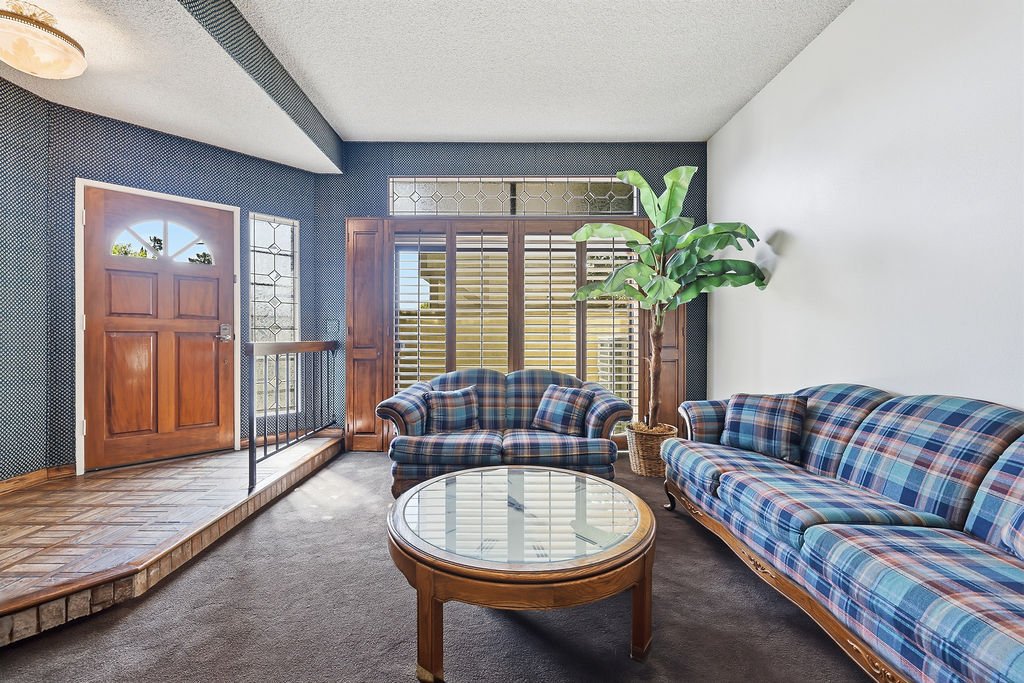 Living room with plaid sofas, a glass coffee table, a large potted plant, and a wooden front door with a window.