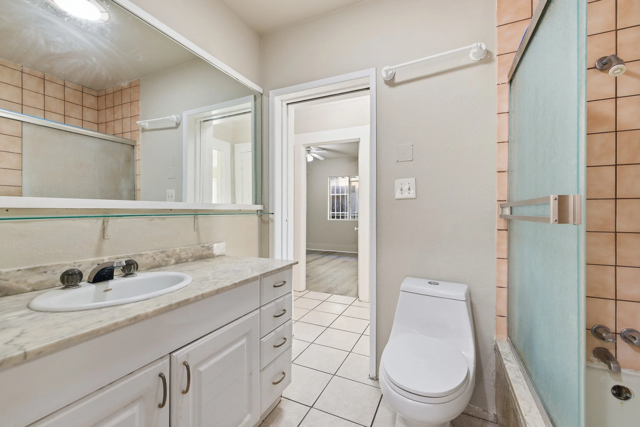 A bathroom with a white vanity and marble countertop, a white sink, a mirror, a toilet, a shower with a partial glass door, and tiled walls and floor.