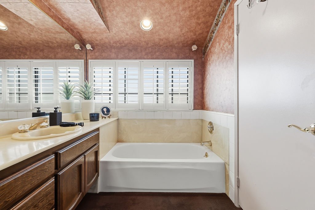 Bathroom with a bathtub, vanity with a sink, and window with white shutters.