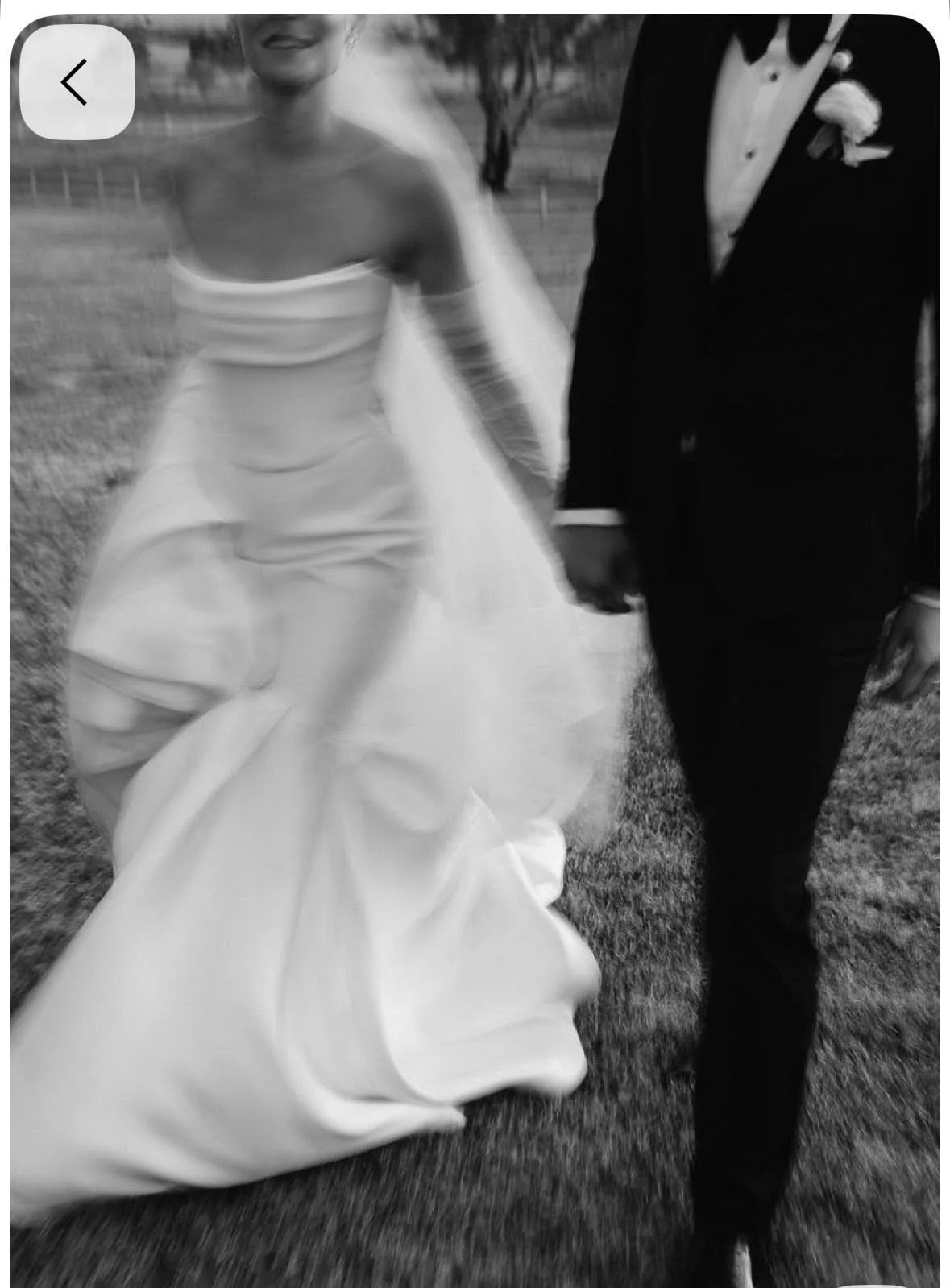 Ein Brautpaar beim Spaziergang im Freien, die Frau trägt ein Hochzeitskleid und der Mann einen schwarzen Anzug.