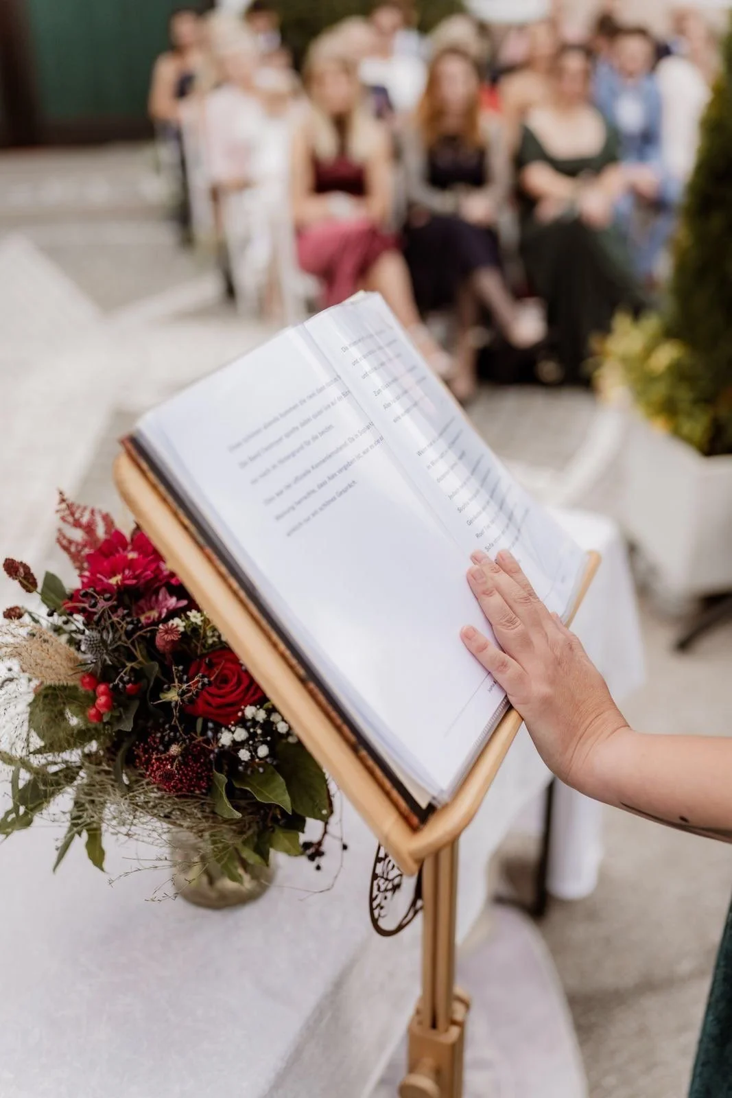 Ein Buch wird vorgelesen bei einer Veranstaltung im Freien, mit einem Publikum im Hintergrund.
