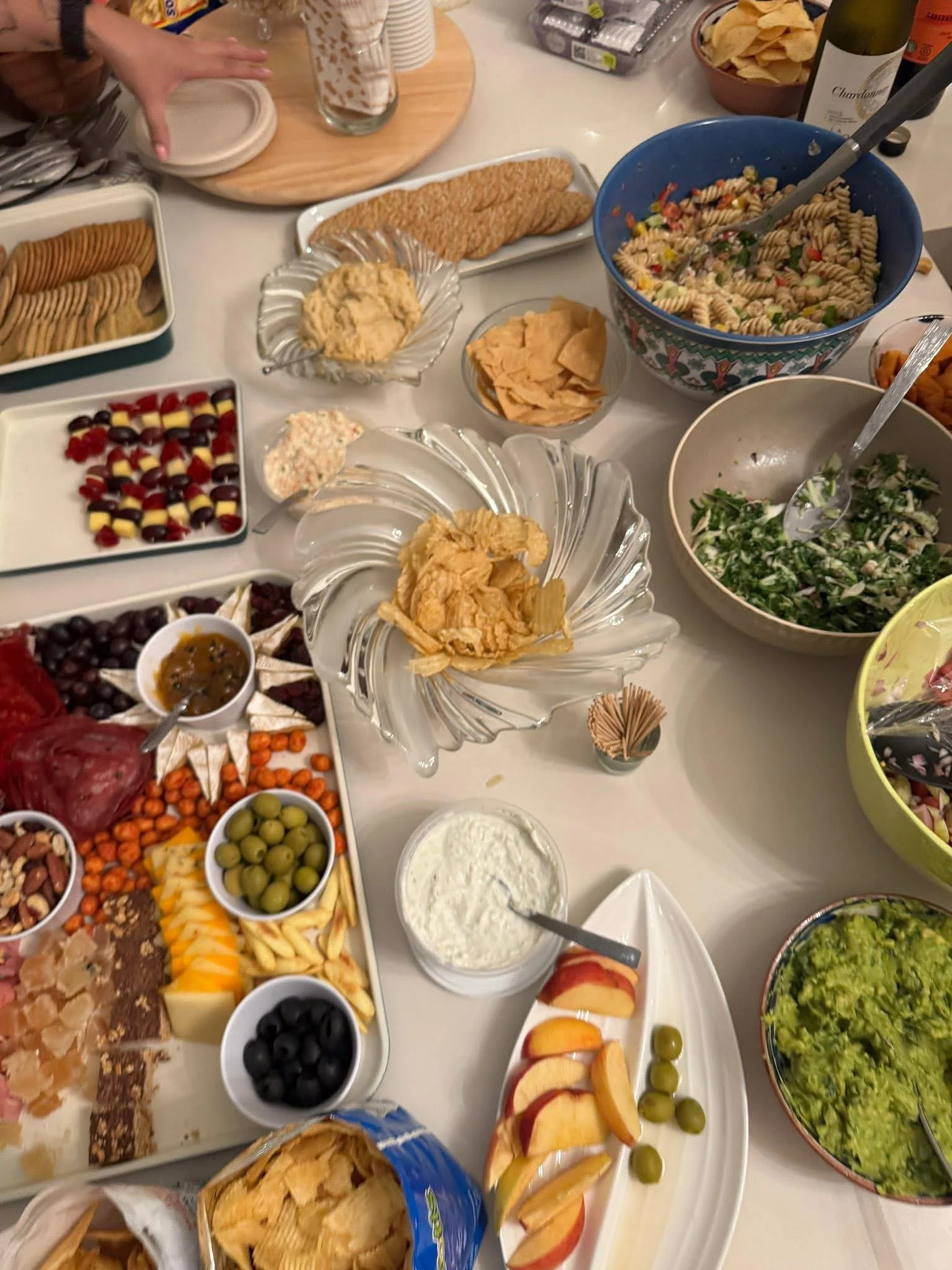 A variety of dishes on a table, including fruit, salads, chips, crackers, and dips.