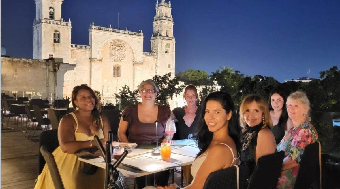Group of women sitting at a table outside during evening with a historic church in the background.