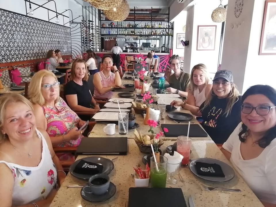 A group of women sitting at a long table in a restaurant, smiling and looking at the camera.