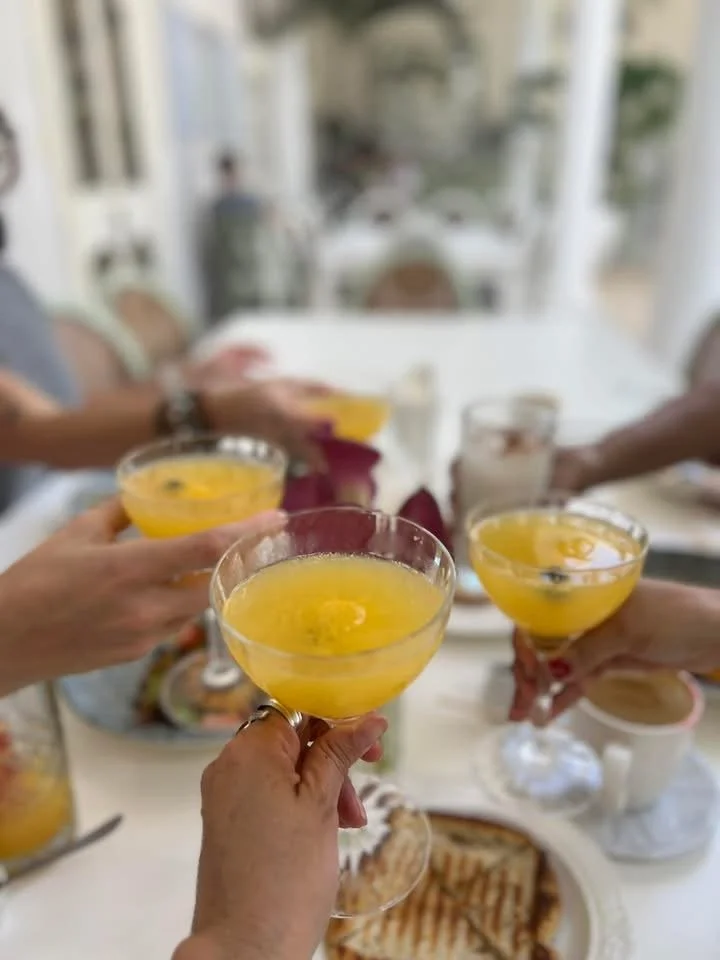 People clinking glasses with yellow cocktails at a dining table with food and drinks.