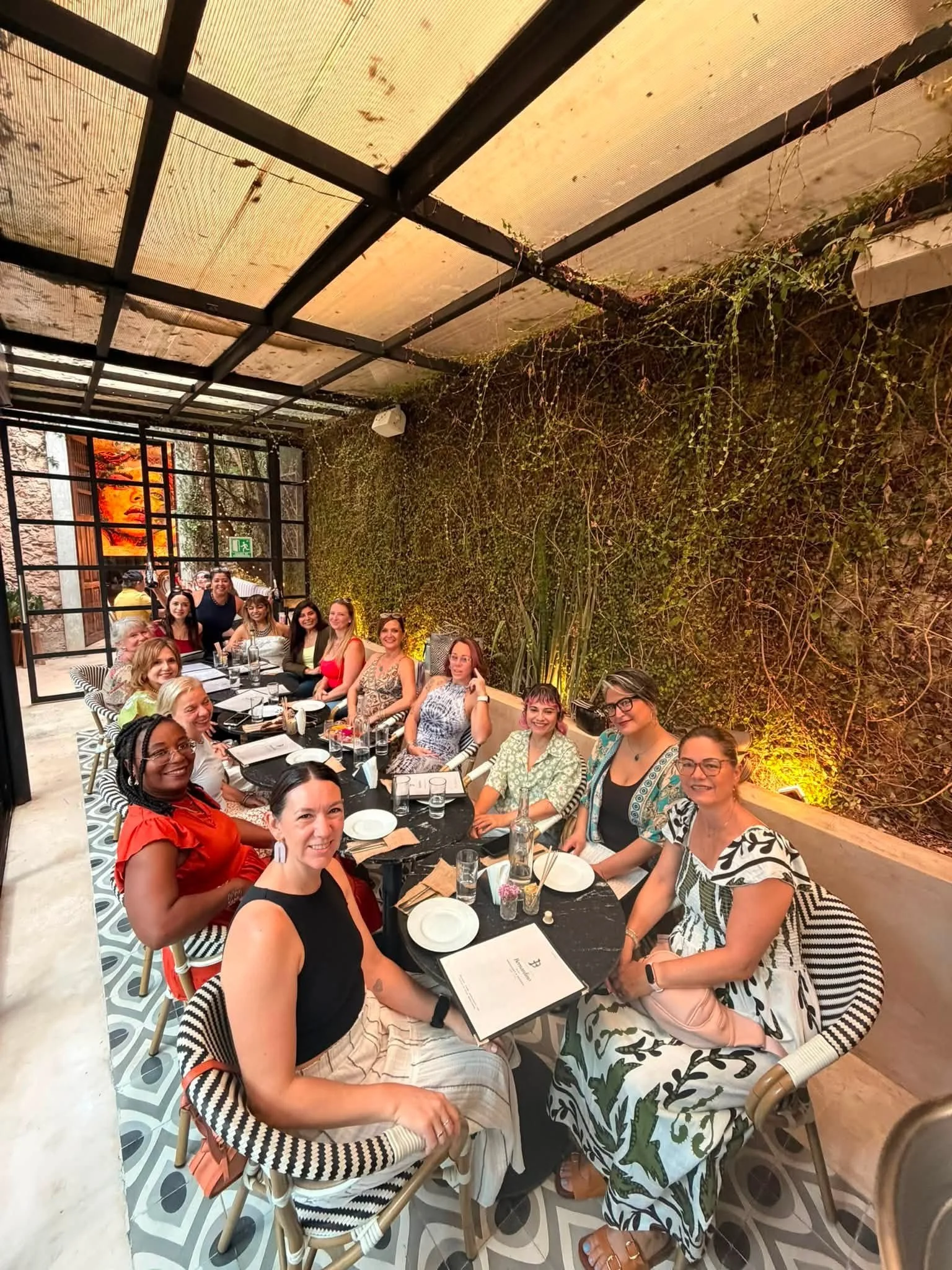 A group of people sitting at a long decorated table in a restaurant with a green plant wall and modern decor.