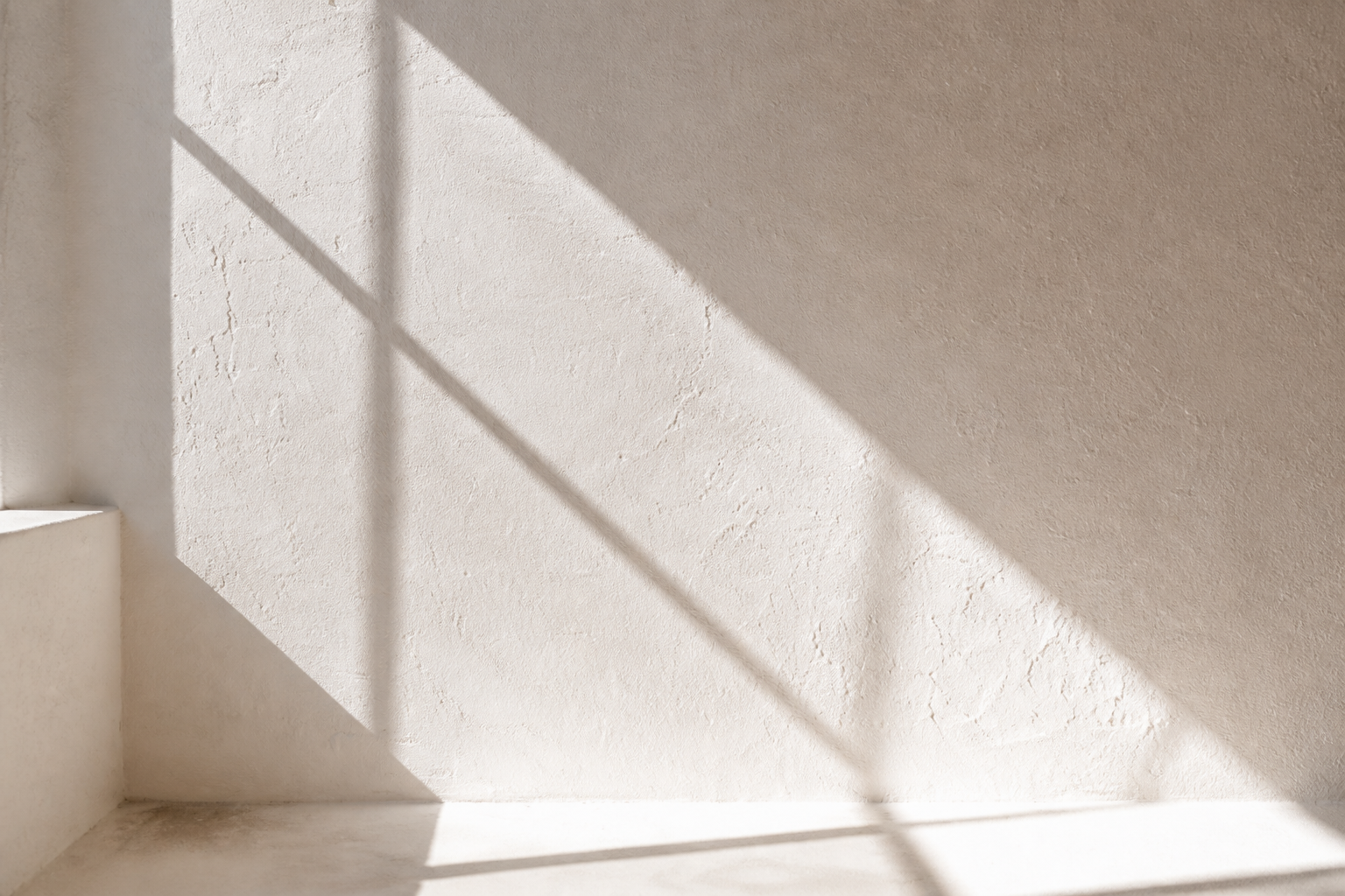 Sunlight casting shadows on a textured white wall and stairs.