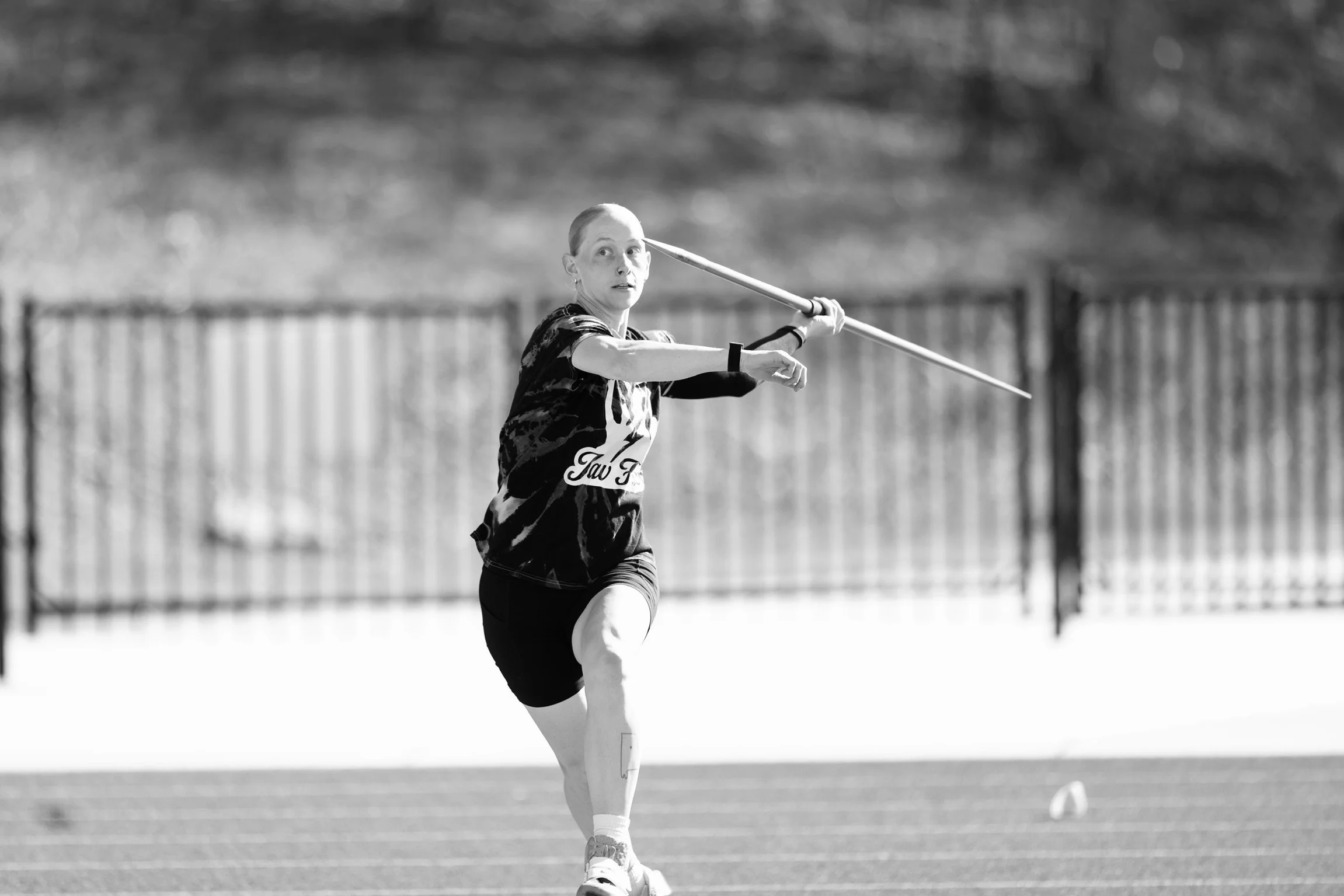 A female athlete with a prosthetic leg running on a track, holding a javelin in an outdoor sports field.