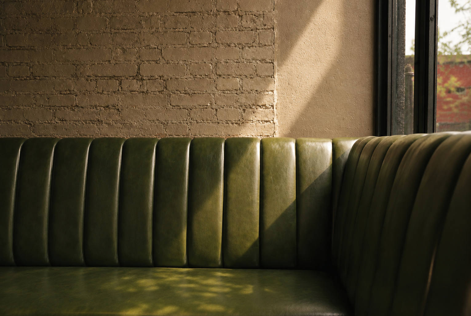 Green leather booth seating next to a window with sunlight casting shadows inside a cafe or restaurant.