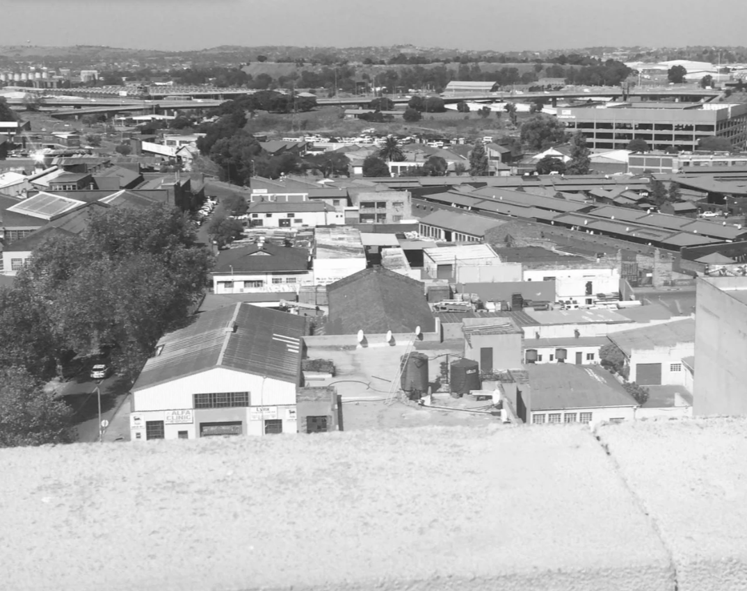 Black and white aerial view of a cityscape with various buildings, trees, and roads extending to the horizon.