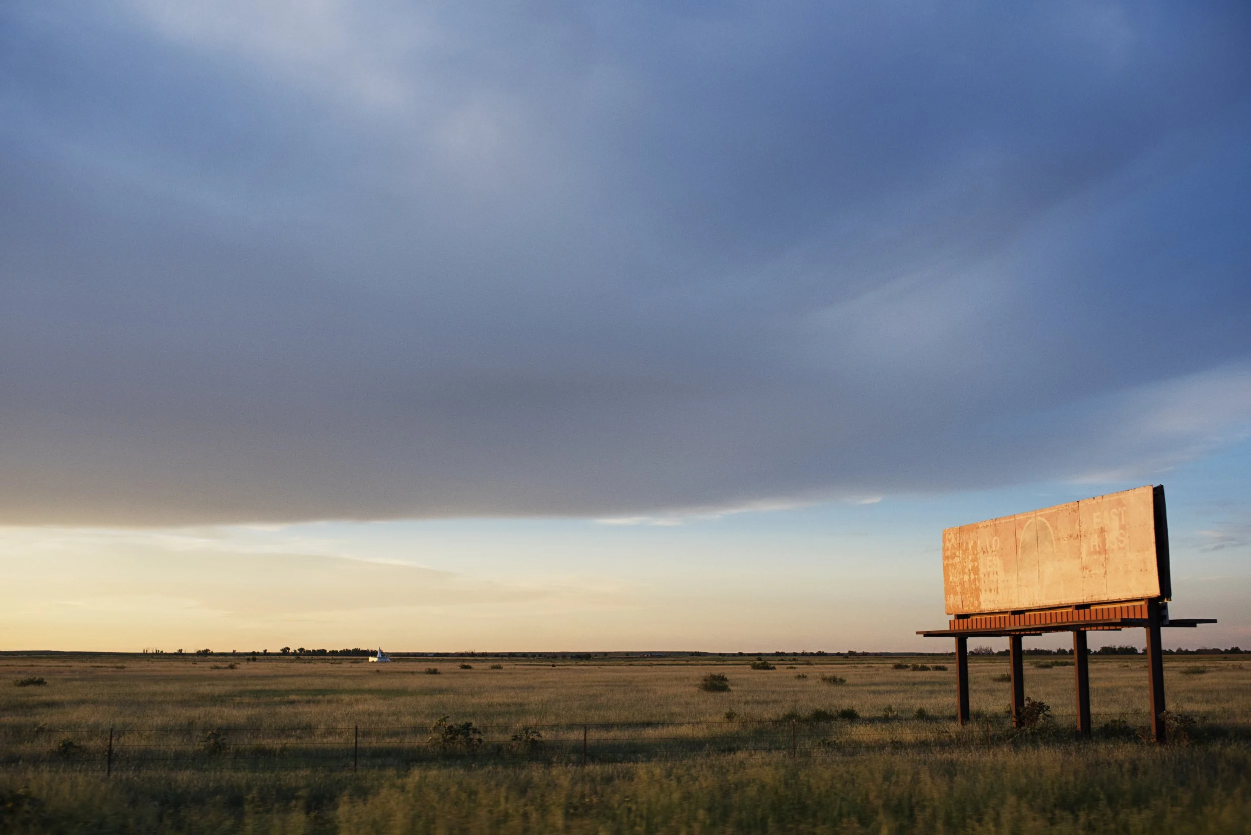 A large, blank billboard in a field under a cloudy sky at sunset.