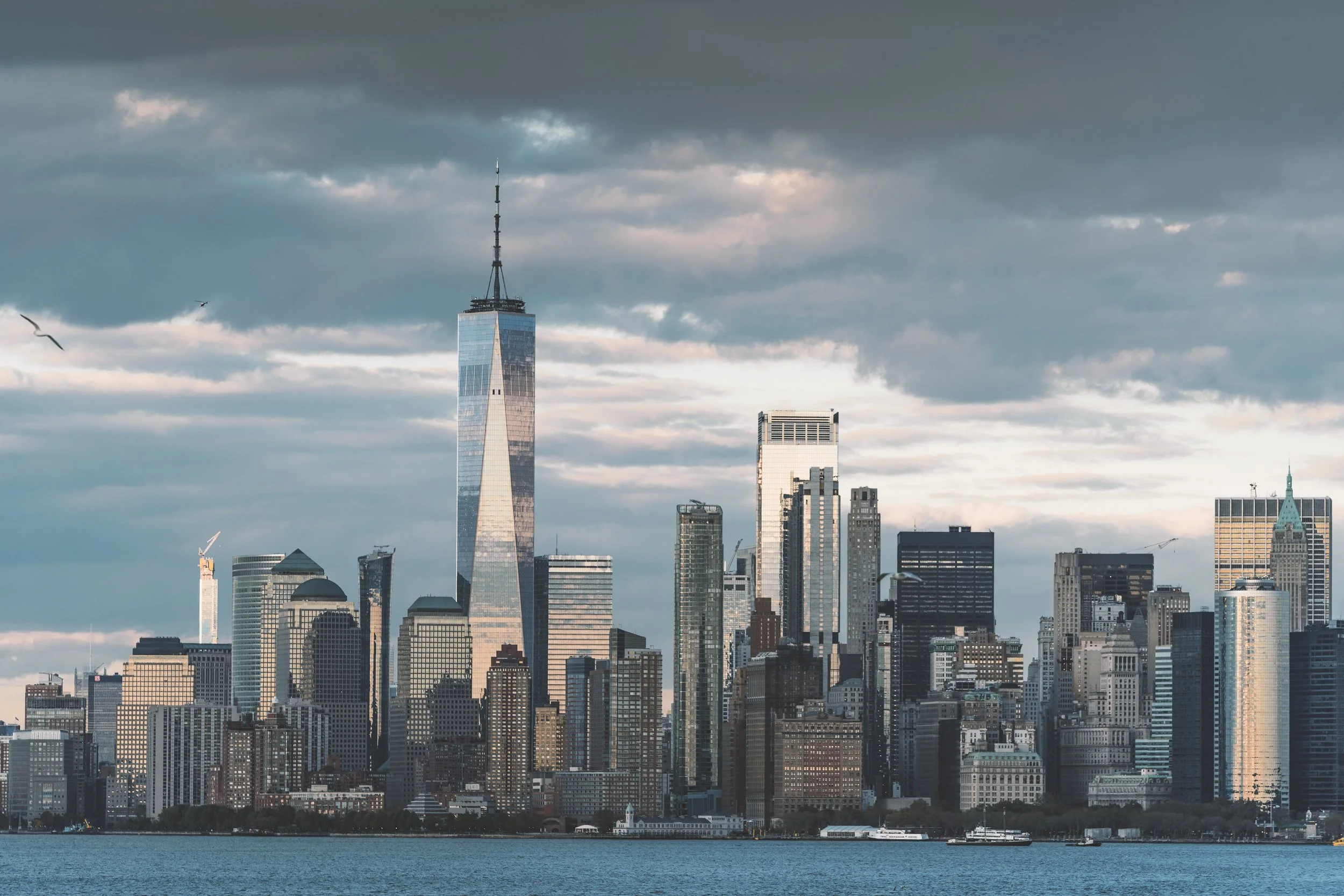 City skyline featuring One World Trade Center with a dark, cloudy sky.