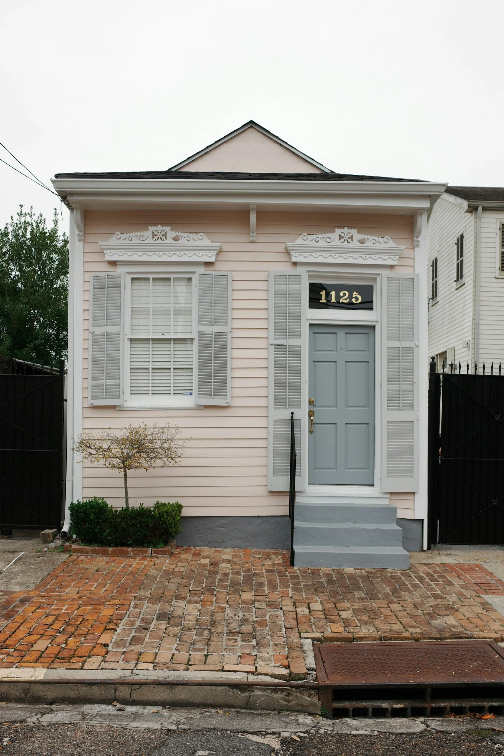 A small single-story house with peach-toned siding, gray shutters, a gray front door, and a brick walkway leading to the entrance
