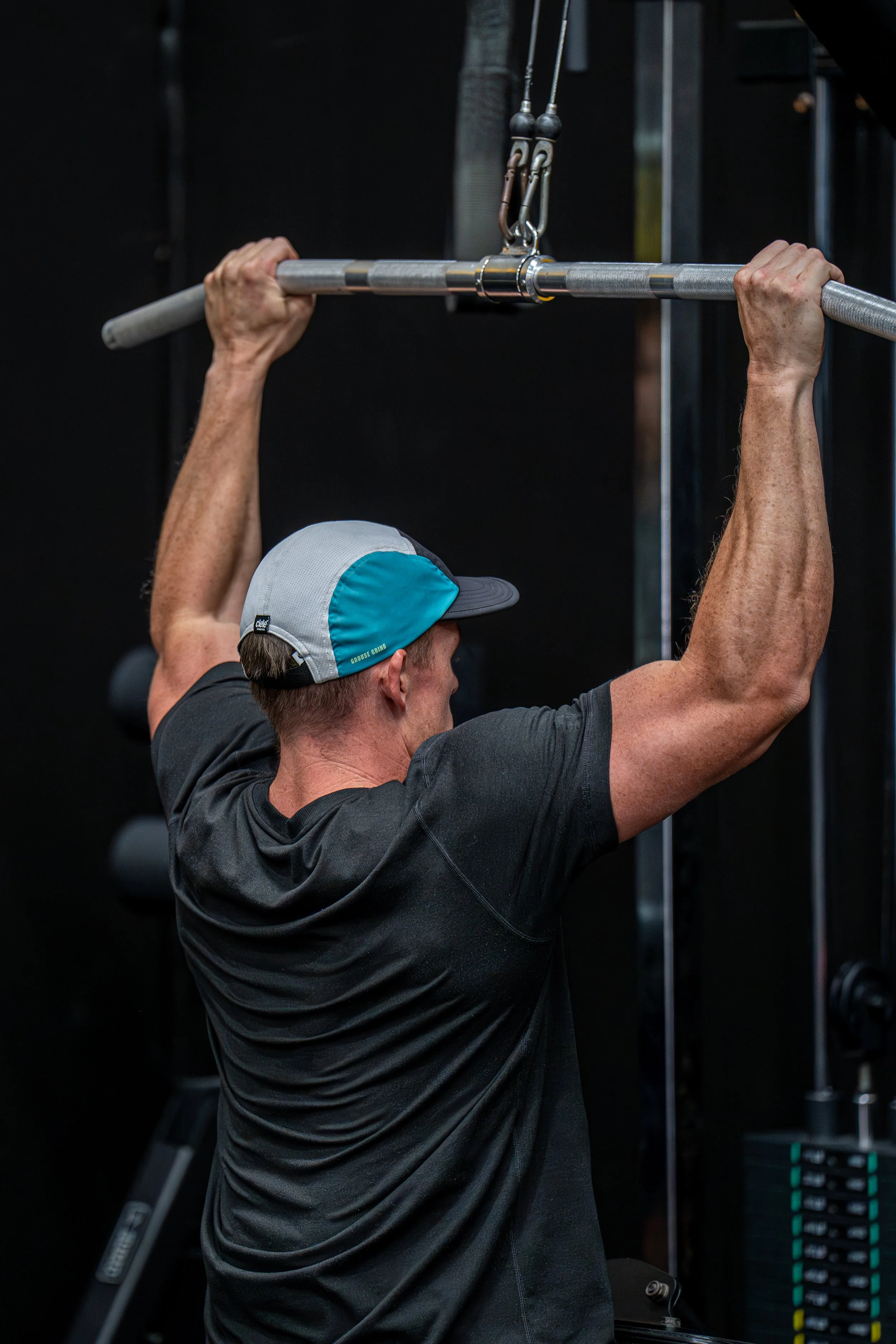 Joe Couch performing a pull-up exercise on a bar in a gym setting.