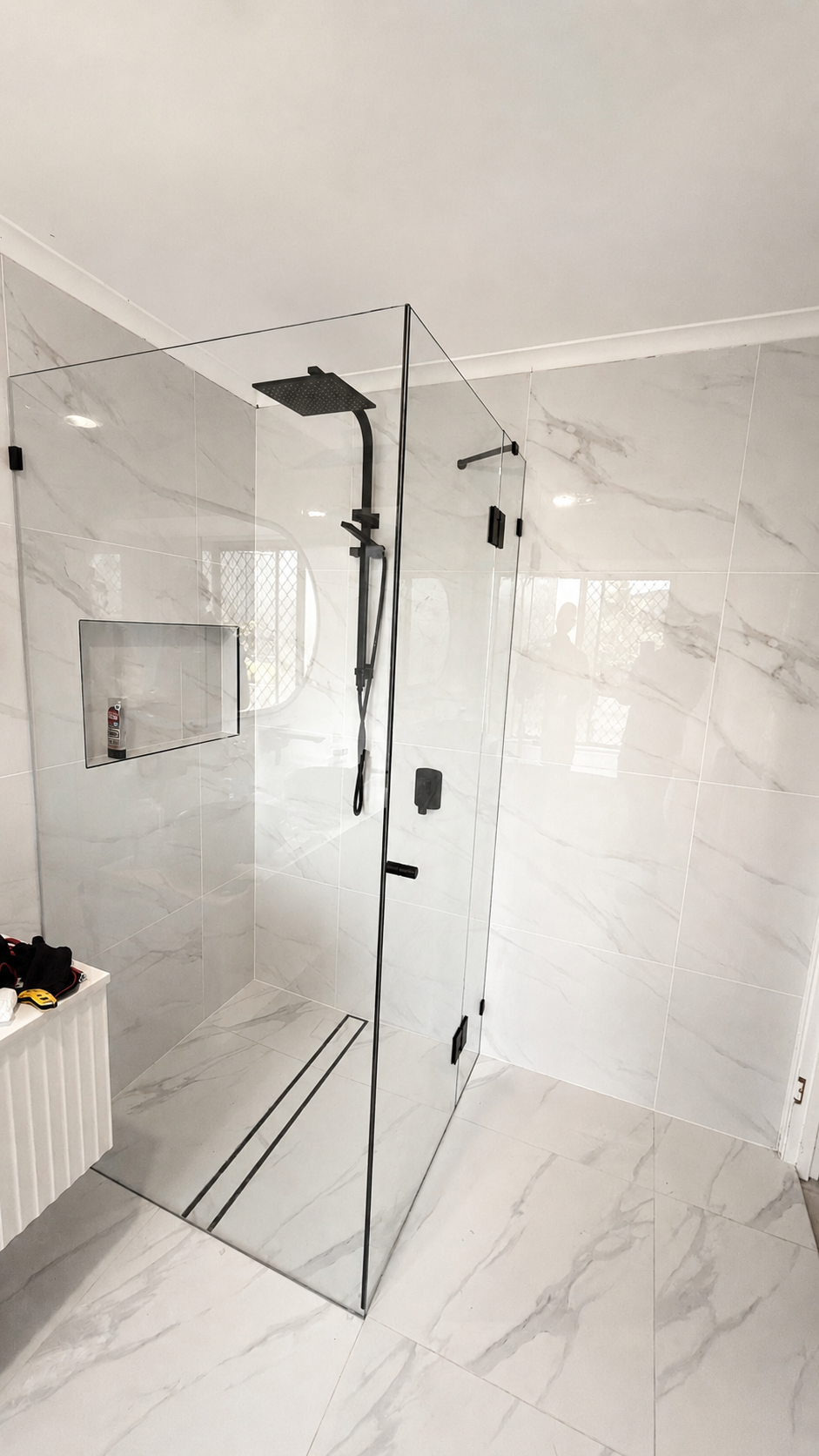 Modern walk-in shower with black fixtures, glass walls, and marble tiles in a bathroom.