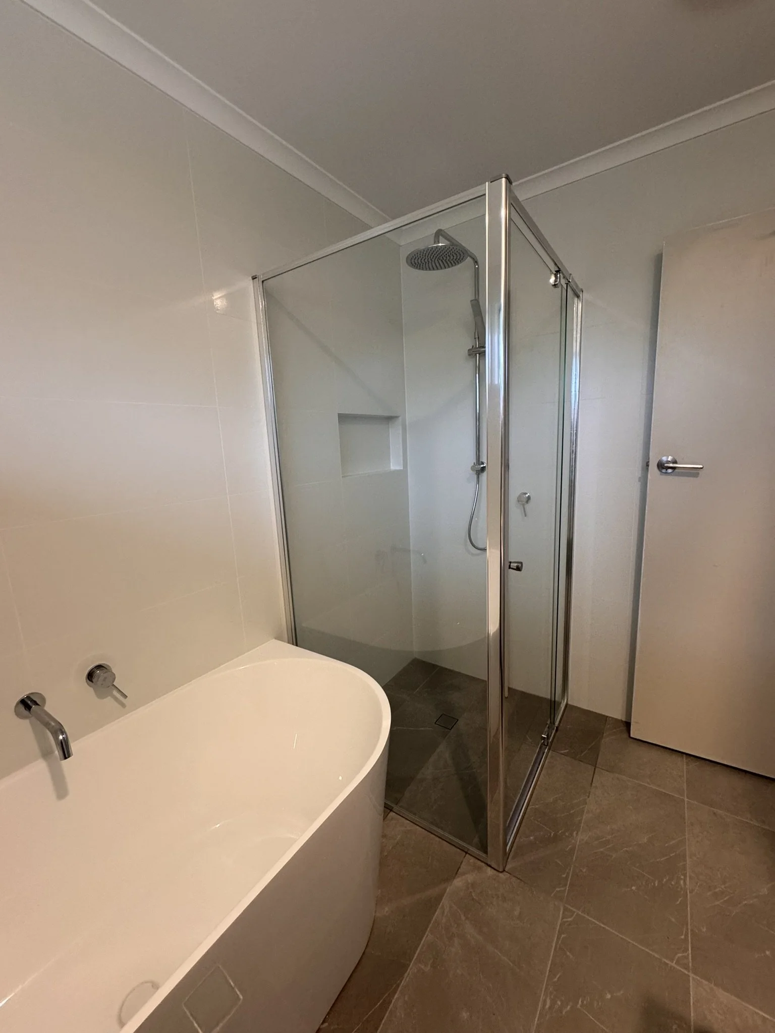 A bathroom with a white bathtub, a glass shower enclosure, and gray tiled flooring.