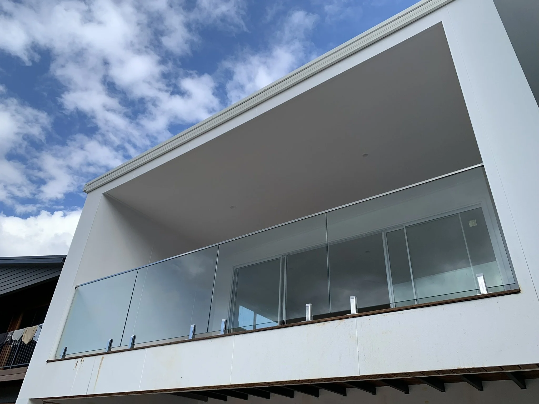 Modern building with white exterior, glass railing balcony, and cloudy blue sky.