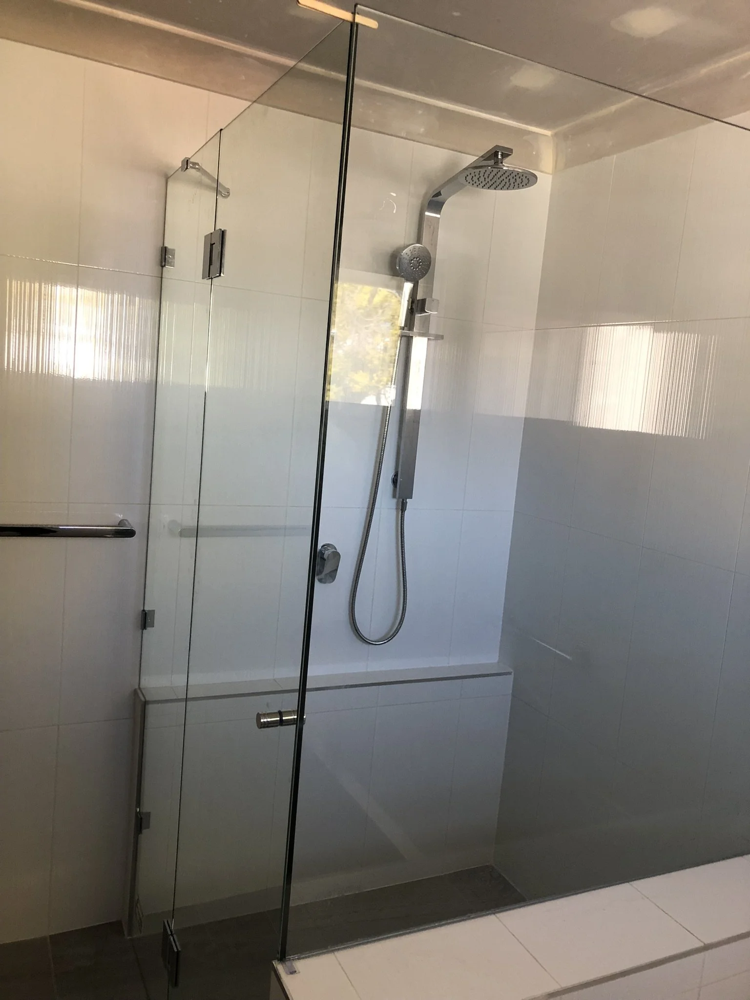 A bathroom shower with a glass door, a handheld showerhead, and a wall-mounted shower panel in a minimalist design.